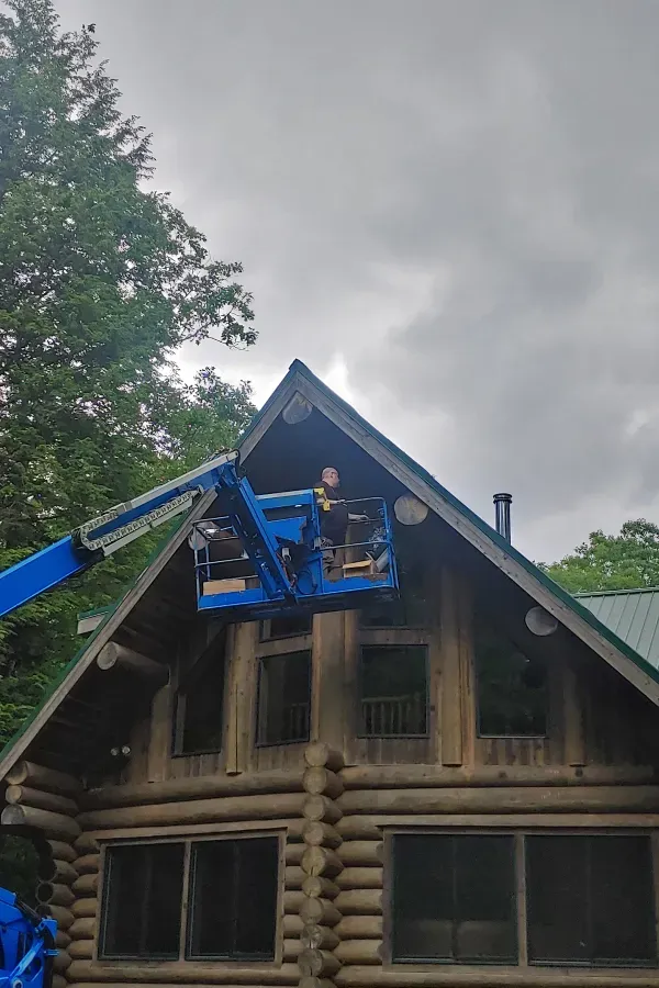 A man is cleaning the roof of a log cabin with a crane.
