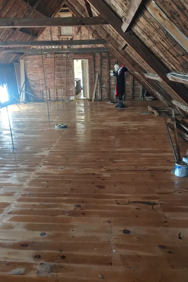 A man is cleaning a wooden floor in an attic.