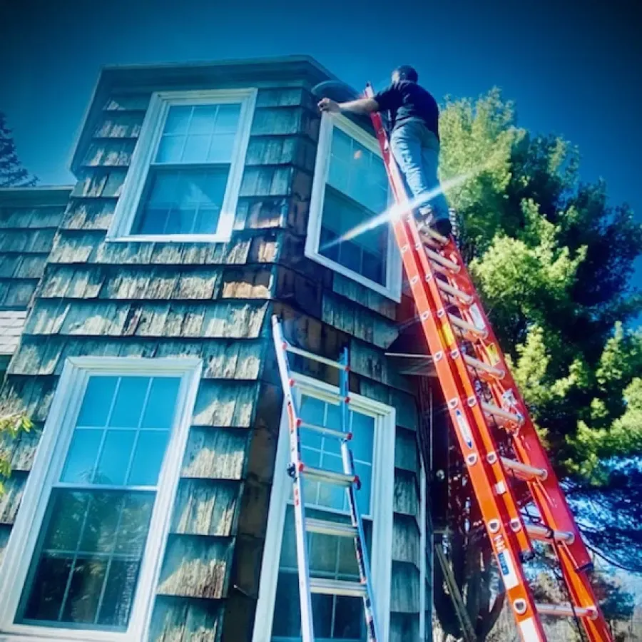 A man on a ladder is installing a window on a house.