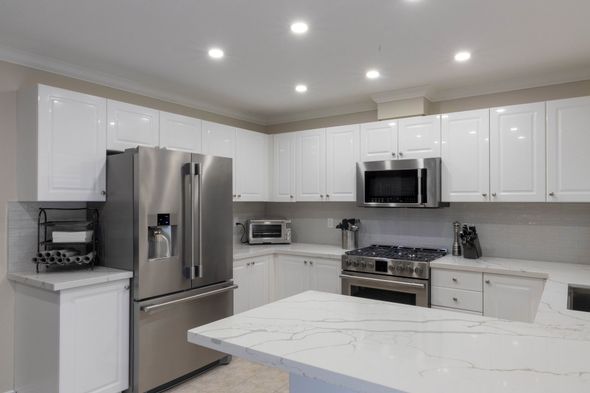 Residential kitchen with new quartz countertops, white cabinets and stainless steel appliances.