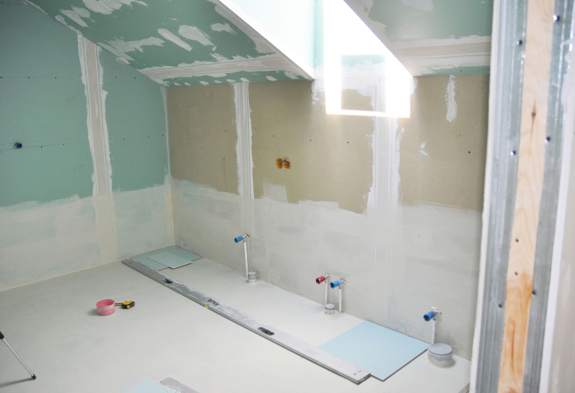 Unfinished bathroom remodel with drywall, exposed plumbing, skylight window, and construction tools.