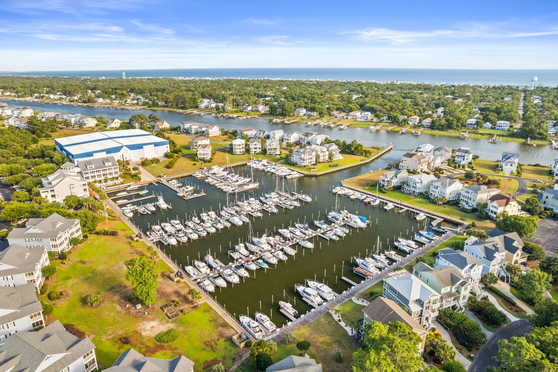 Aerial view of a marina with rows of boats, docks, and waterfront homes under a sunny sky