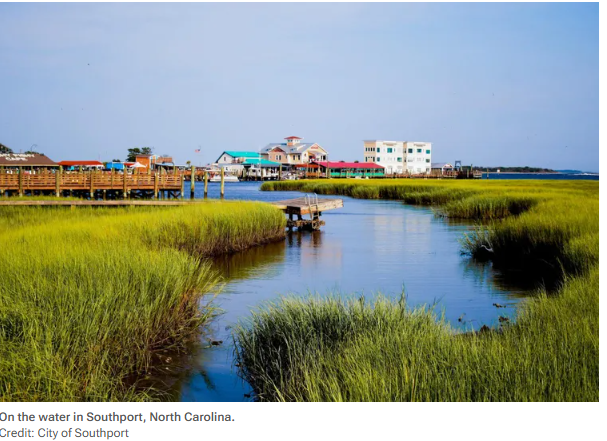 Travel and Leisure Mar 2026 Boardwalk over marsh grass and water in Southport, North Carolina, with waterfront buildings in the distance