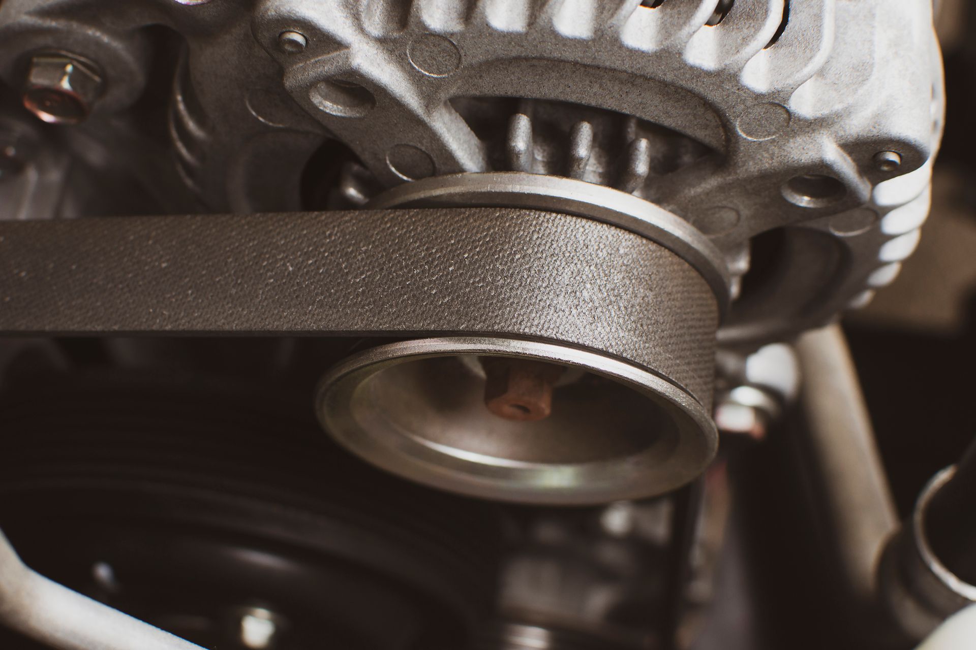 Close-up of a car alternator and pulley with a black belt, part of a vehicle's engine.