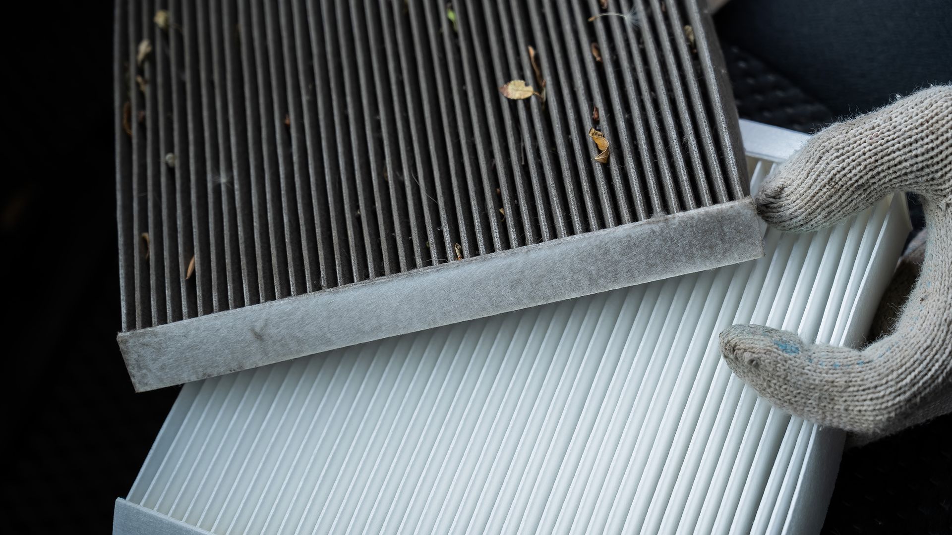 Gloved hand holding a used, dirty air filter next to a new, clean one.