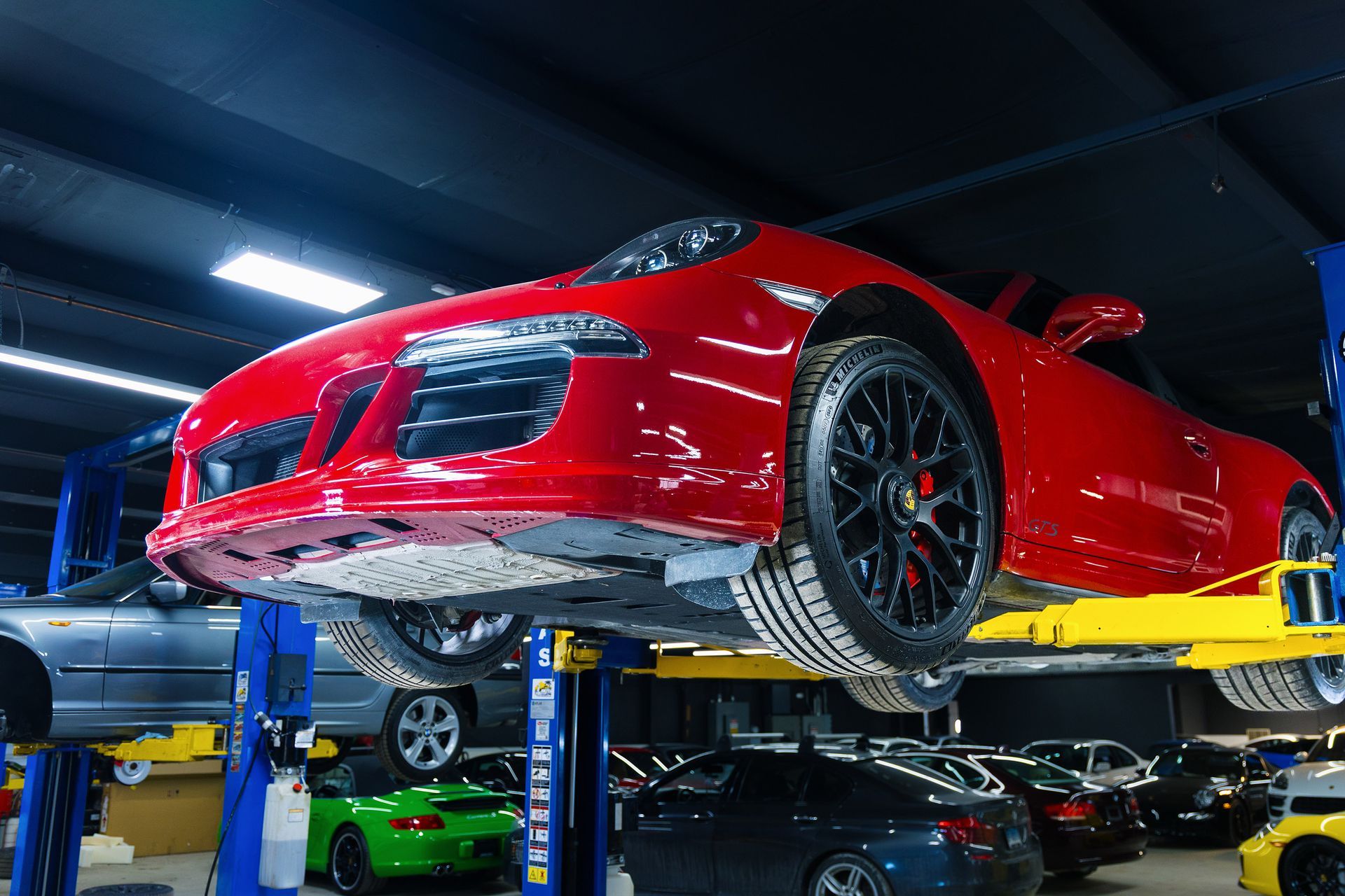 Red sports car on a lift in a garage, black rims, other cars in background.