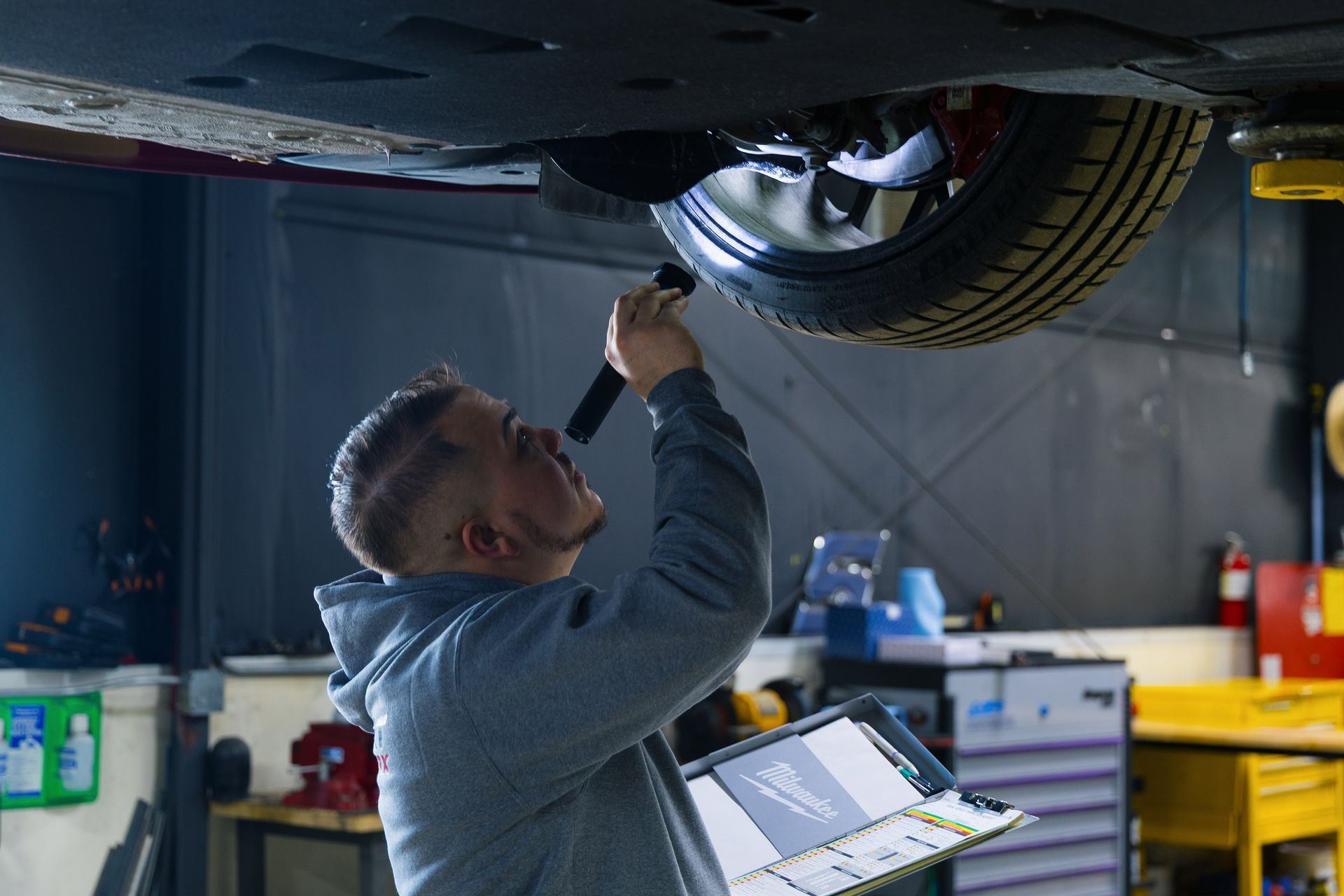 Mechanic examining car undercarriage with a flashlight in a garage.