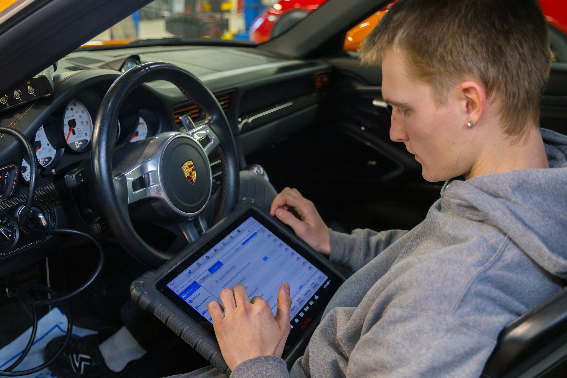 Man in a gray hoodie using a tablet inside a car, for diagnostics.