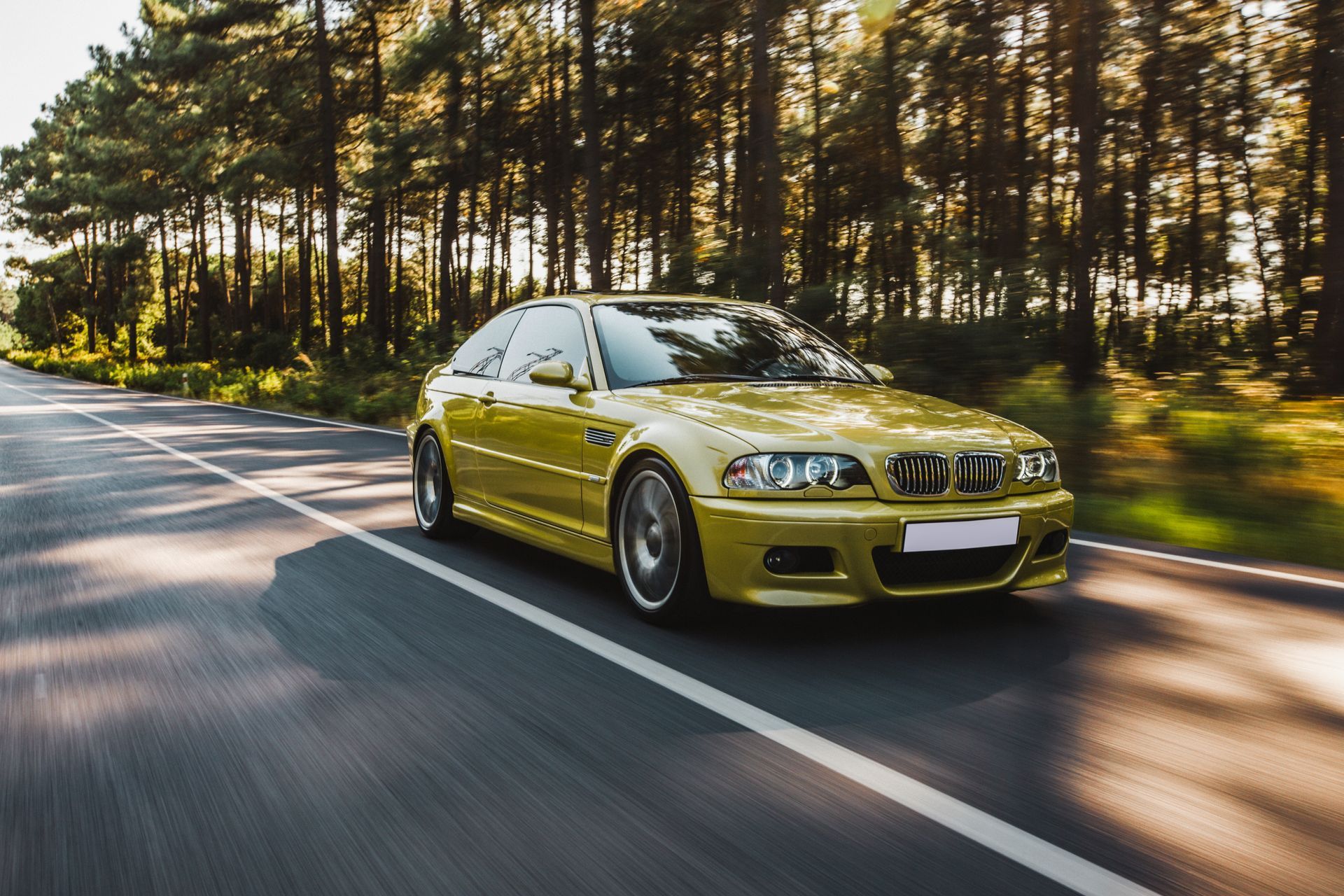 Yellow BMW sports car driving on a tree-lined road.