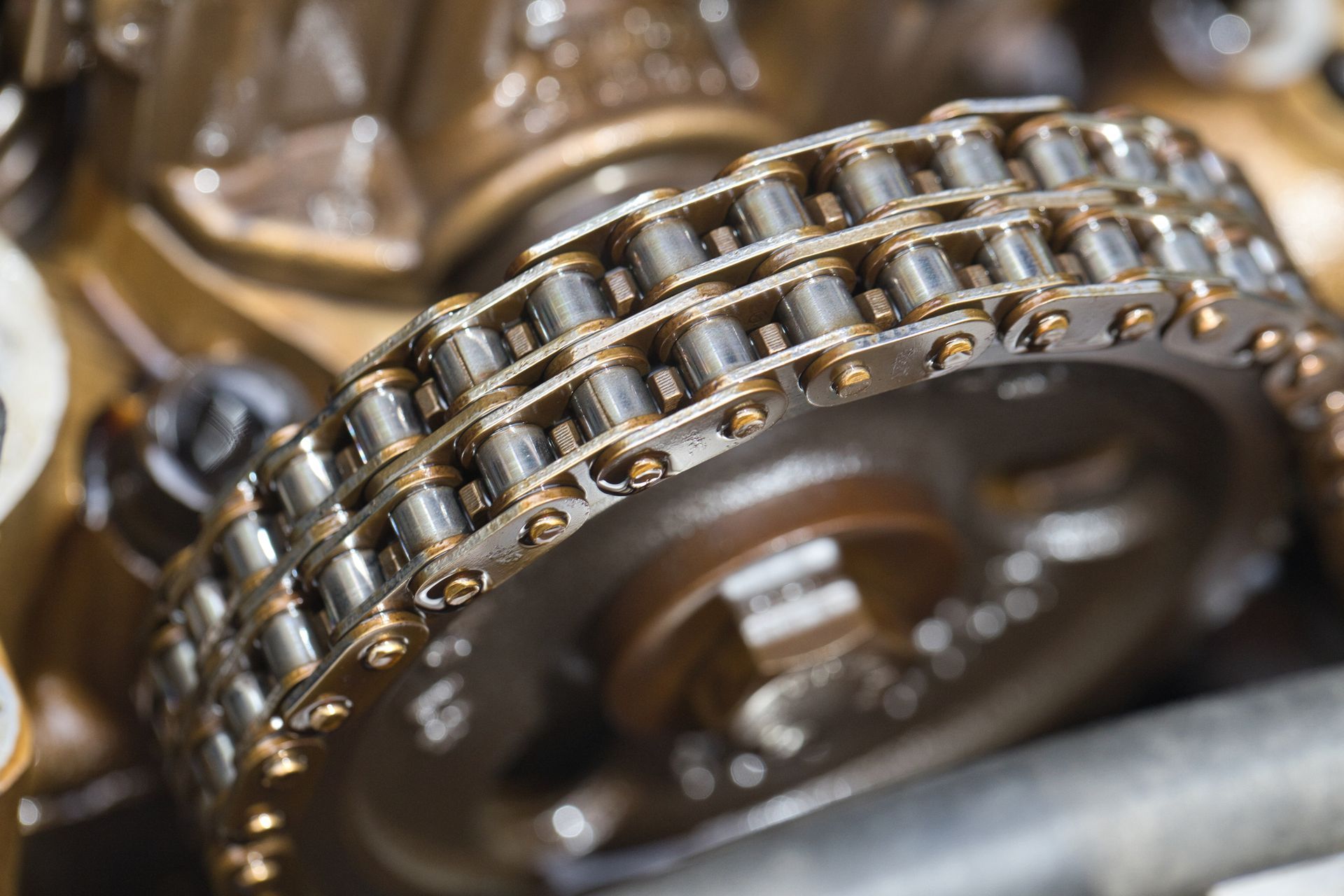 Close-up of a timing chain and gear inside an engine, metallic and brown colors.
