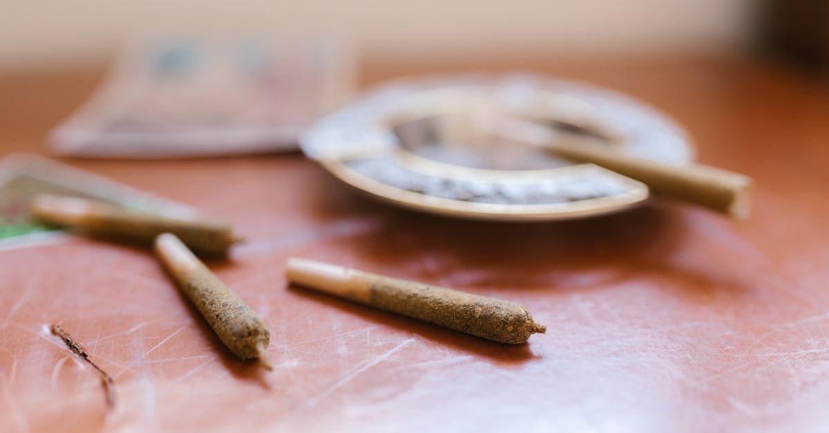 Three joints are sitting on a wooden table next to an ashtray.