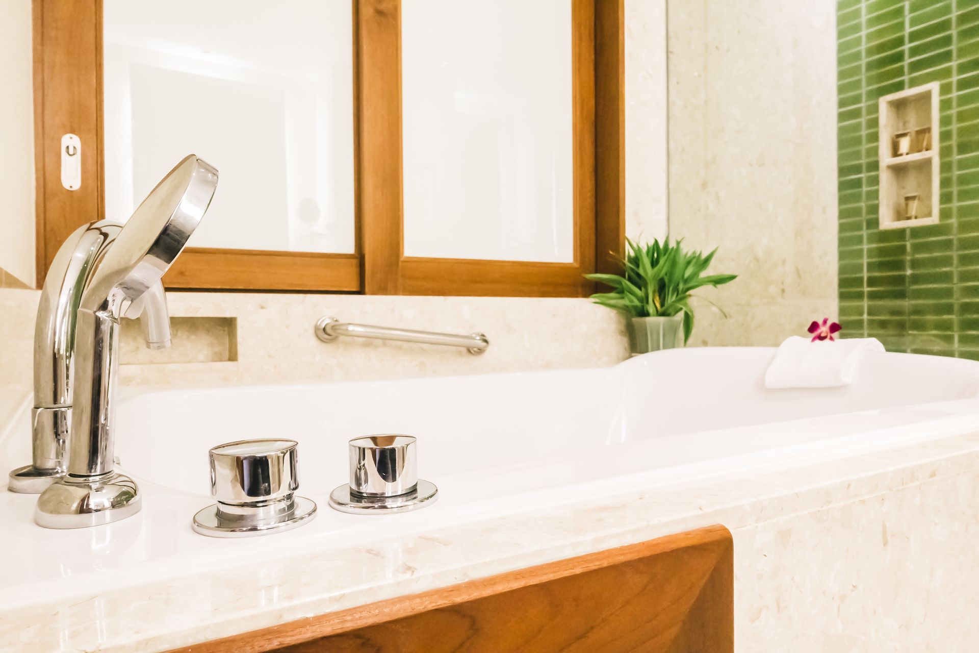 A white bathtub with chrome fixtures, a small green plant, and a folded towel with a flower in a bright, modern bathroom.