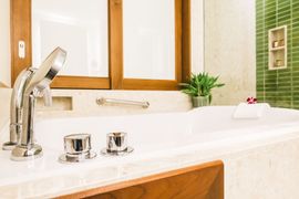 A white bathtub with chrome fixtures, a wooden window frame, a small green plant, and a green tiled wall in a bathroom.