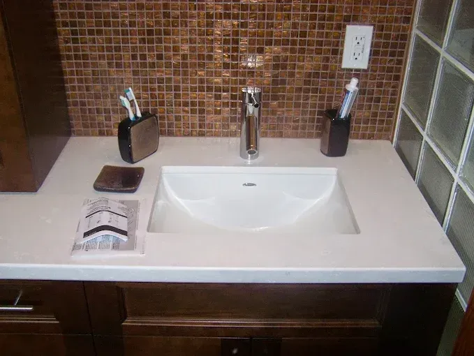 A bathroom vanity with a white sink, chrome faucet, and bronze mosaic tile backsplash.