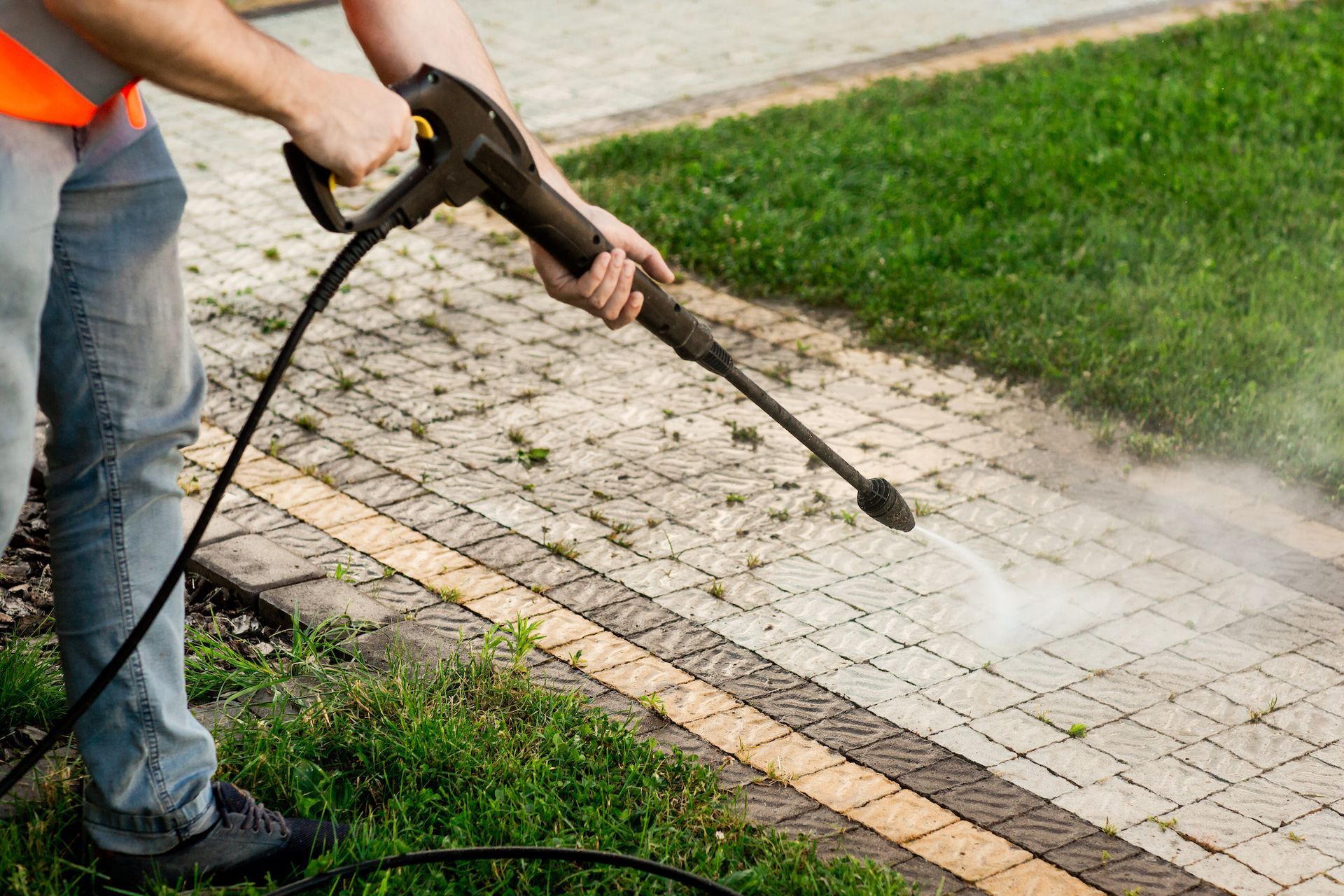 A man is using a high pressure washer to clean a sidewalk.