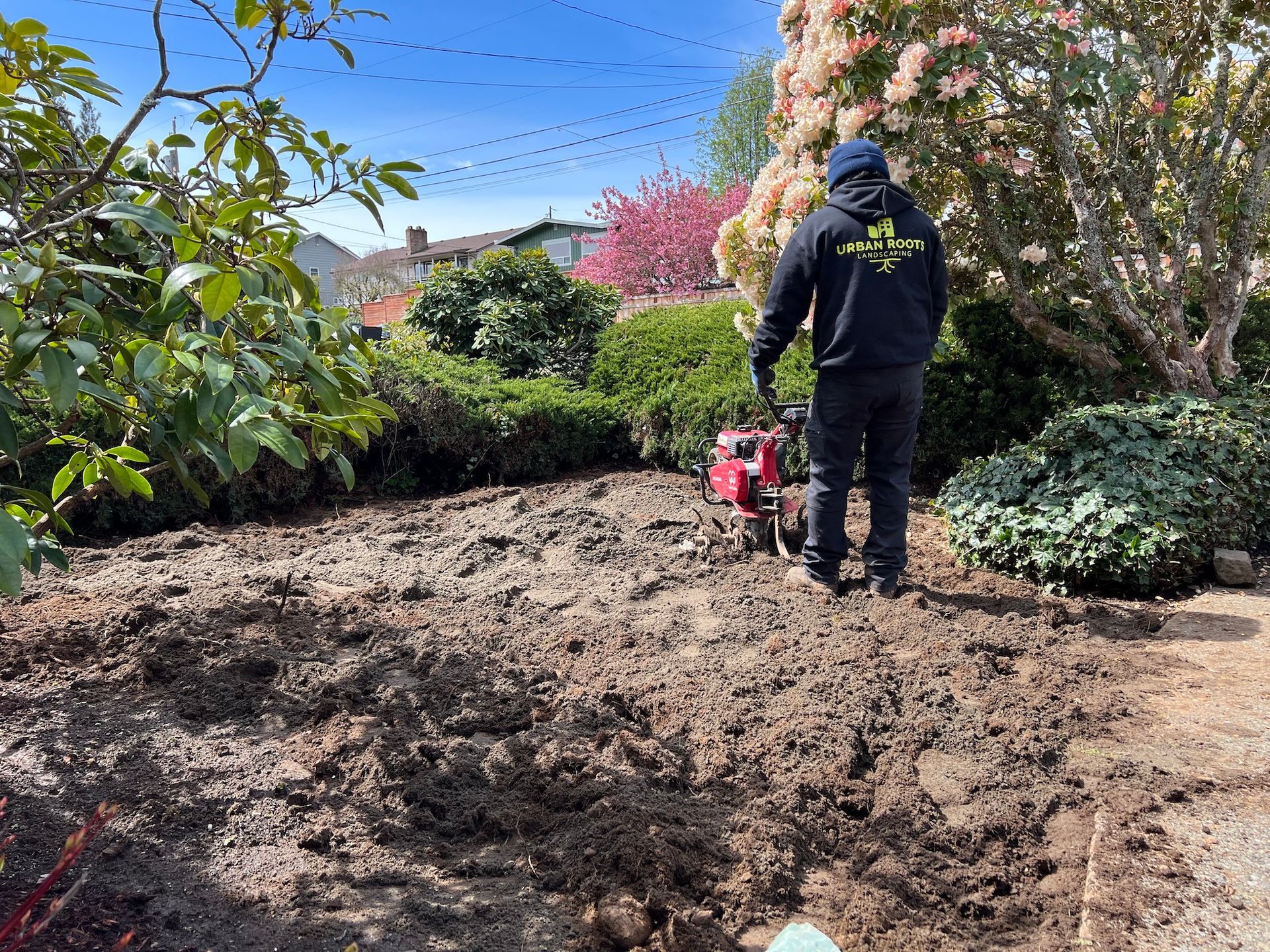 A man is standing in the dirt in a garden holding a small machine.