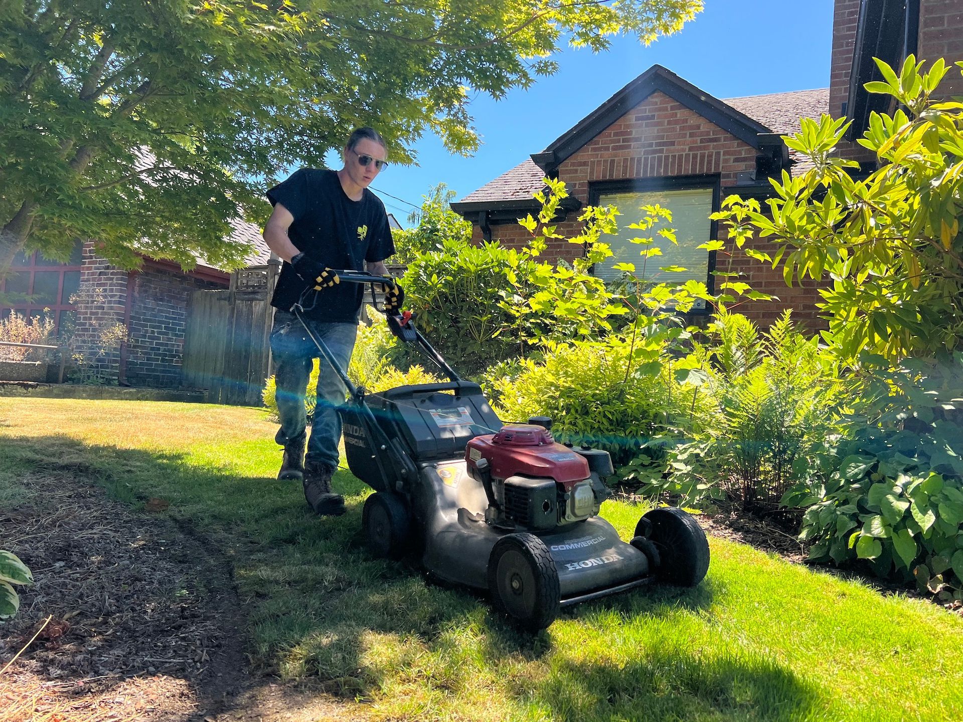 A man is standing next to a lawn mower in front of a house.