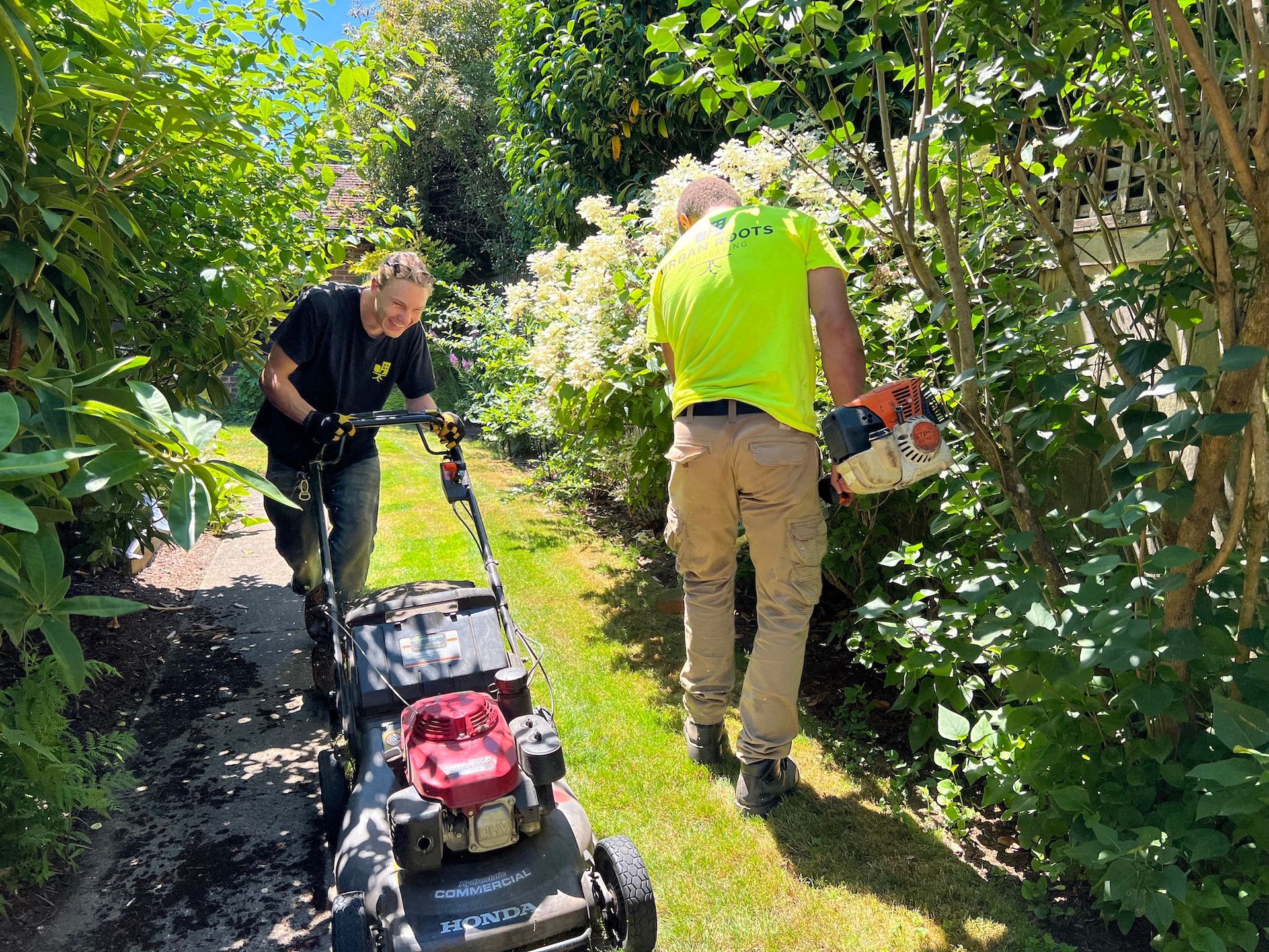 Two men are mowing a lawn with a lawn mower.