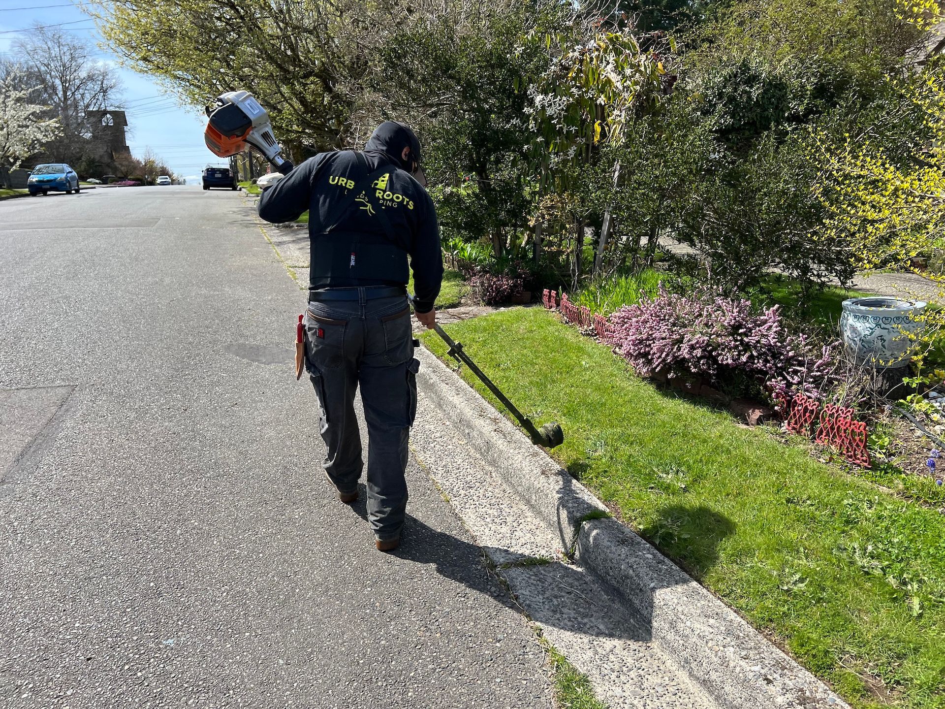 A man is walking down the street holding a lawn mower.