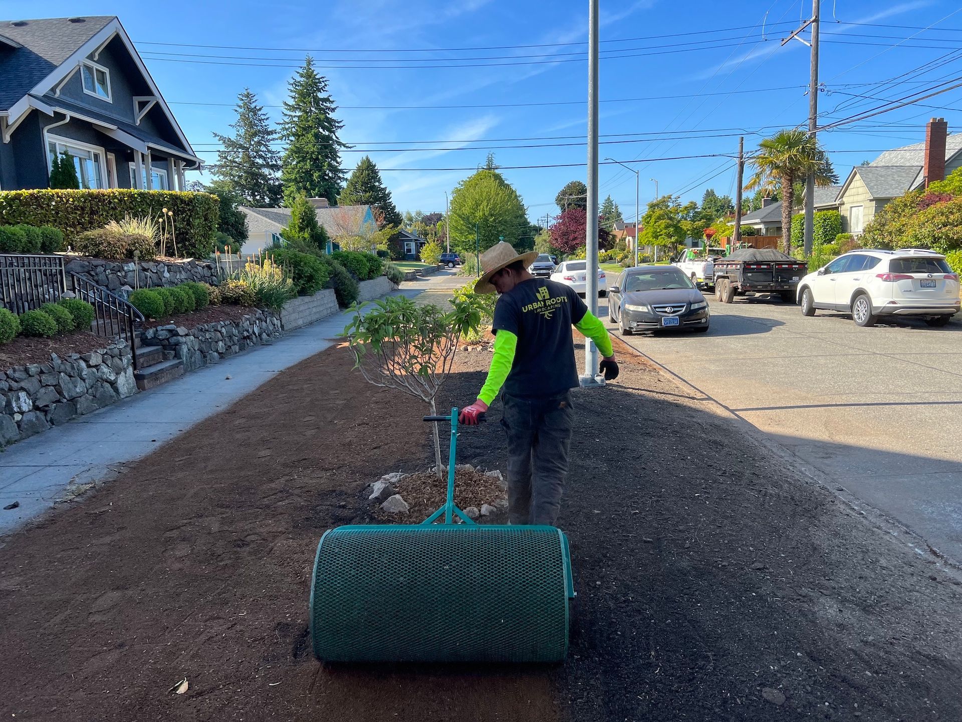 A man is using a roller to roll dirt on the side of the road.