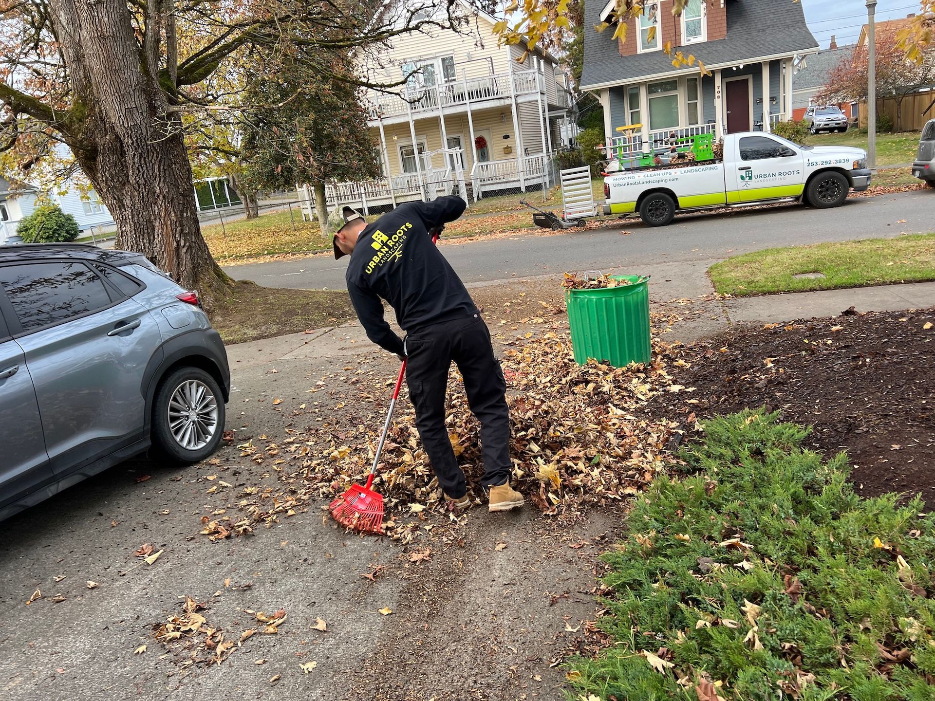 A man is raking leaves on the side of the road.