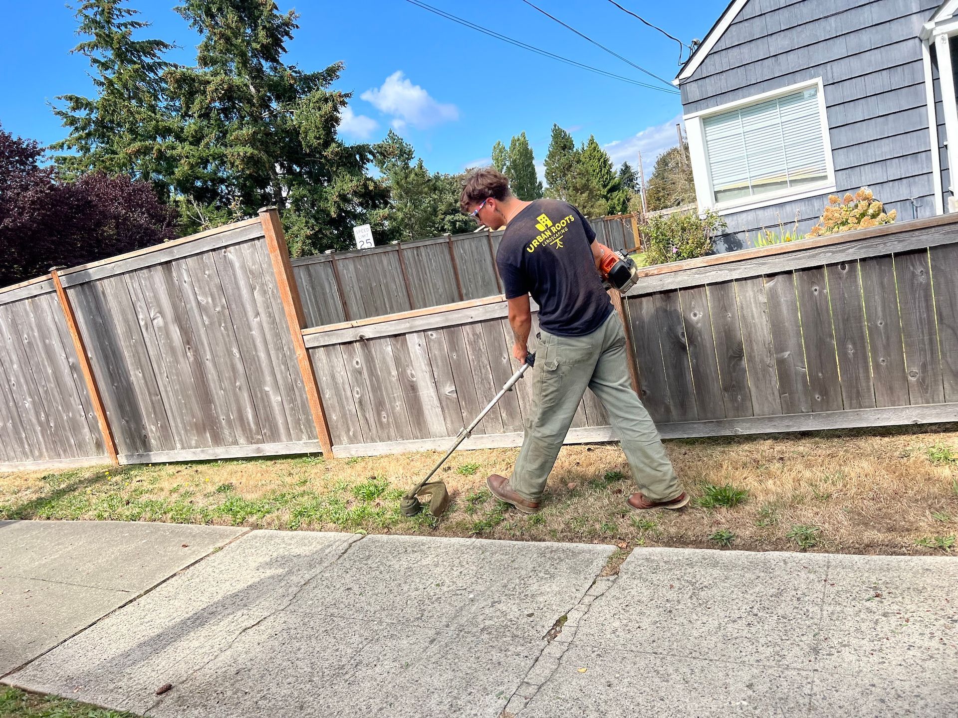 A man is mowing the grass in front of a wooden fence.