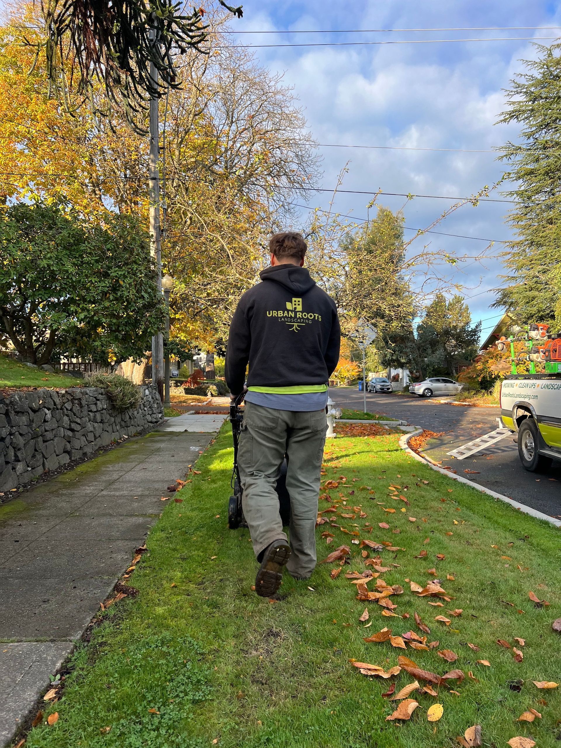 A man is walking down a sidewalk with a leaf blower.