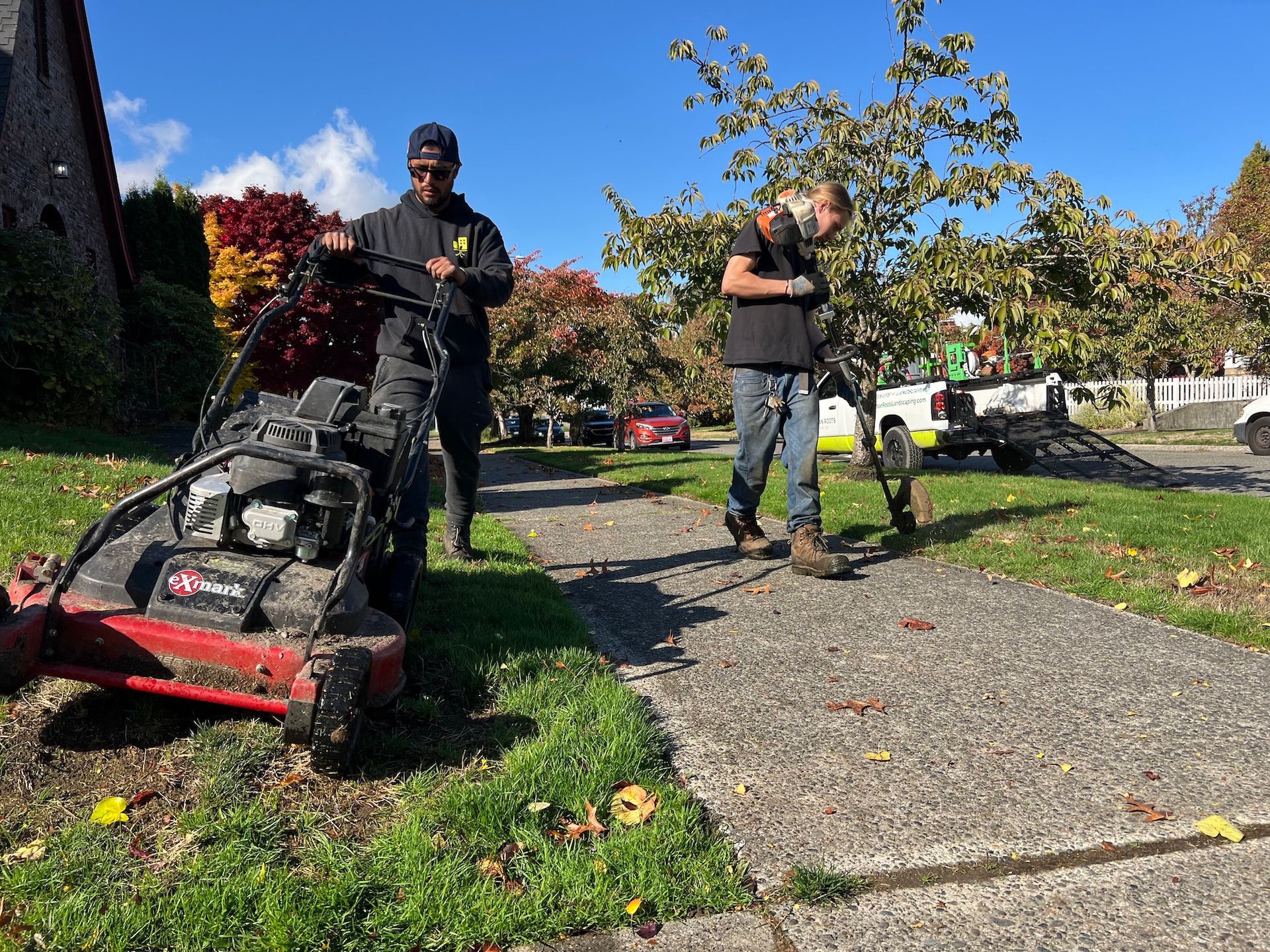 Two men are standing next to a lawn mower on a sidewalk.