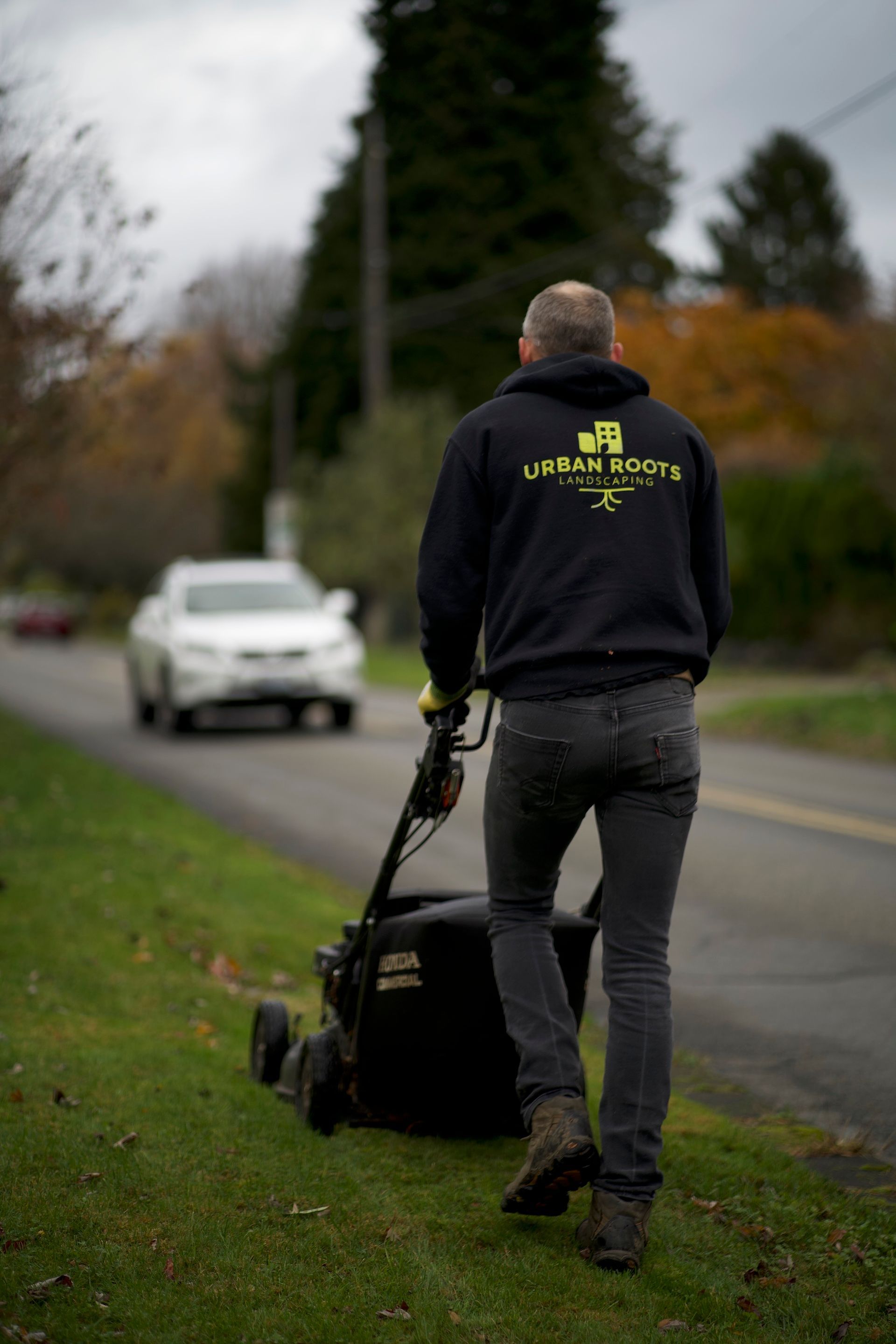 A man is pushing a lawn mower down the side of a road.