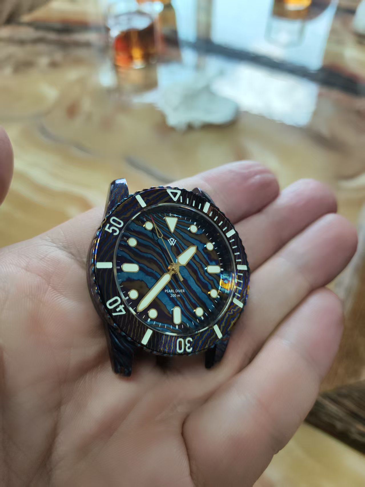 Close-up of a watch dial with a blue and brown wave pattern, held in a person's hand.