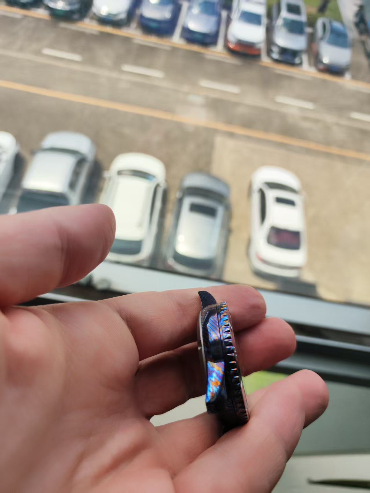 Hand holding a black and blue watch with a parking lot in the background.