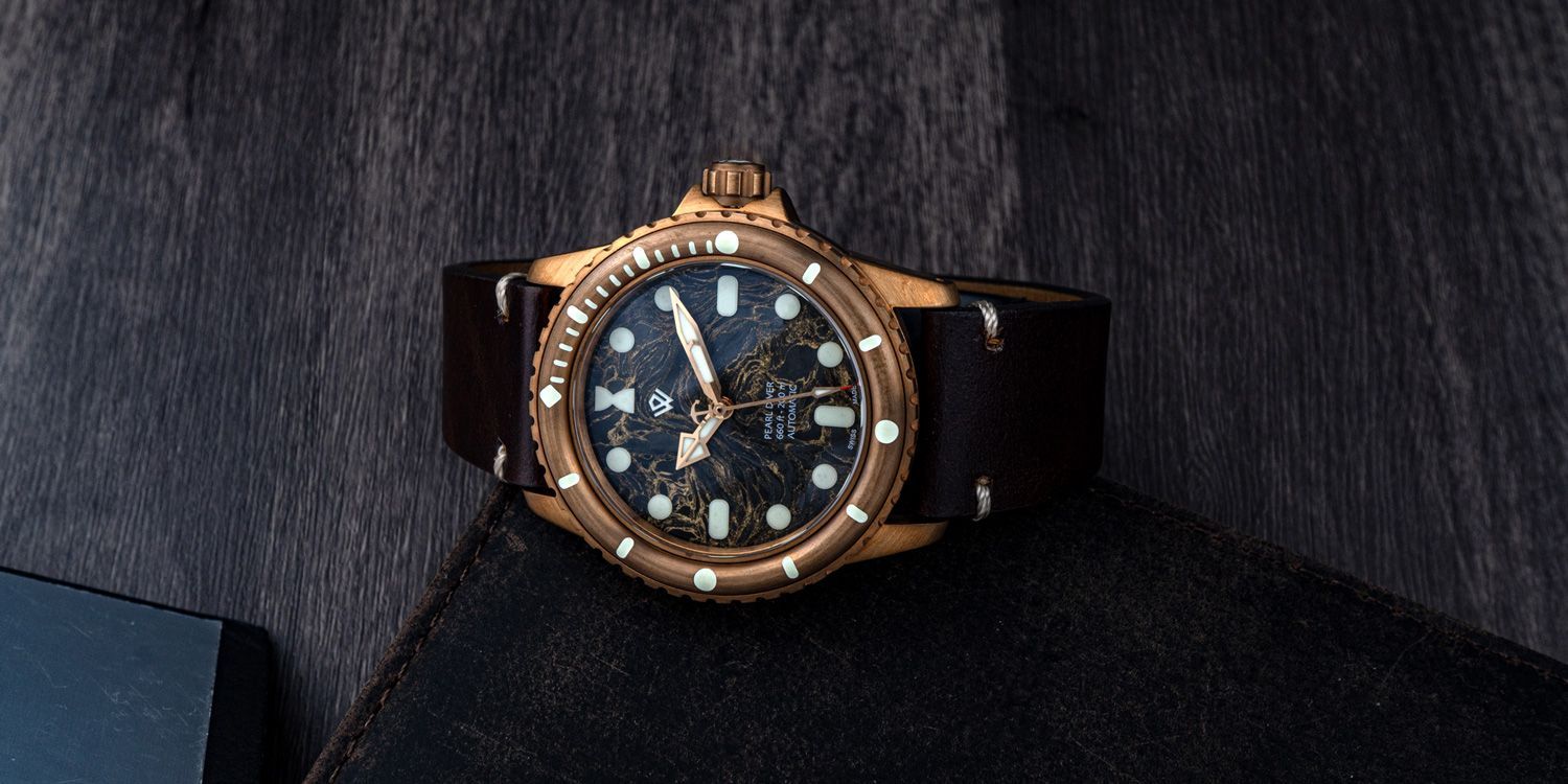Bronze watch with a dark leather strap on a textured black surface.