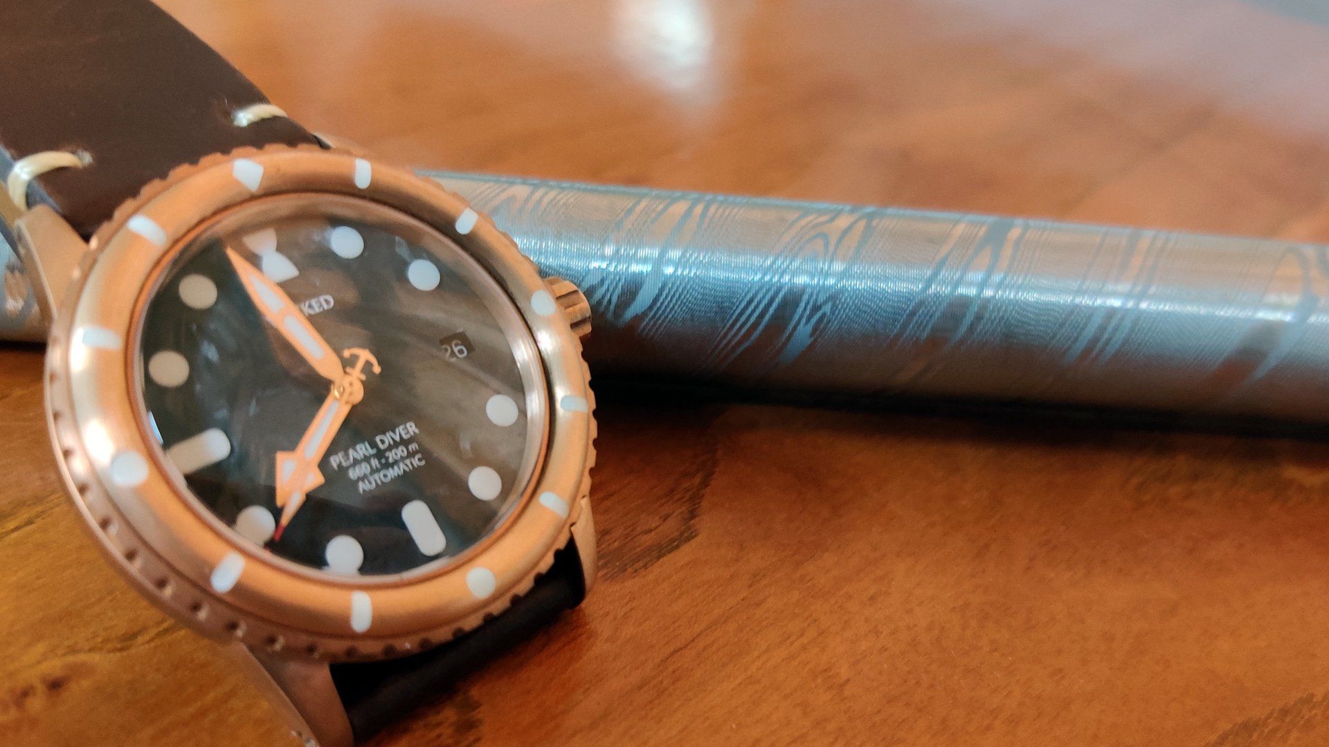 A watch is sitting on a wooden table next to a pen.