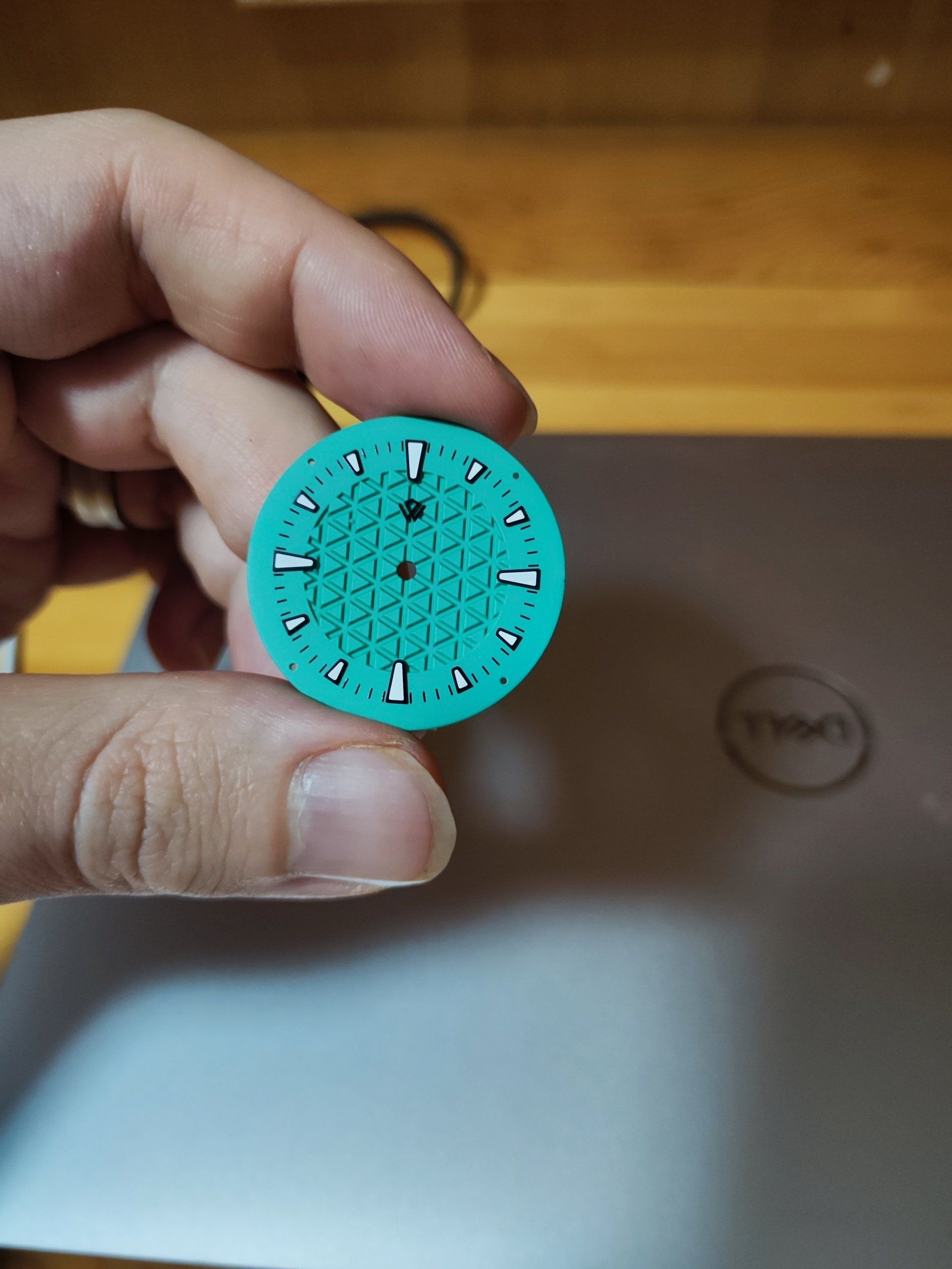 A person is holding a watch face in front of a dell laptop