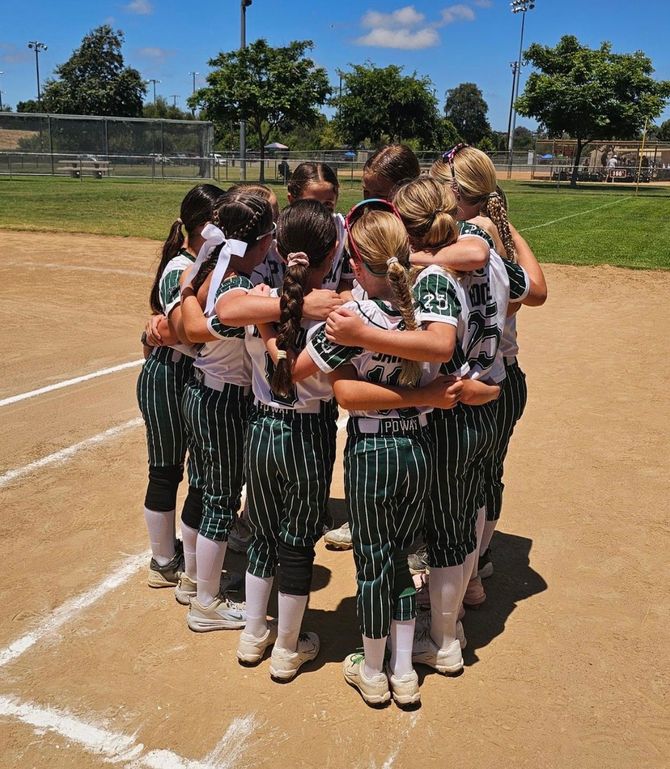 Image with a group of softball player girls huddled together on the field