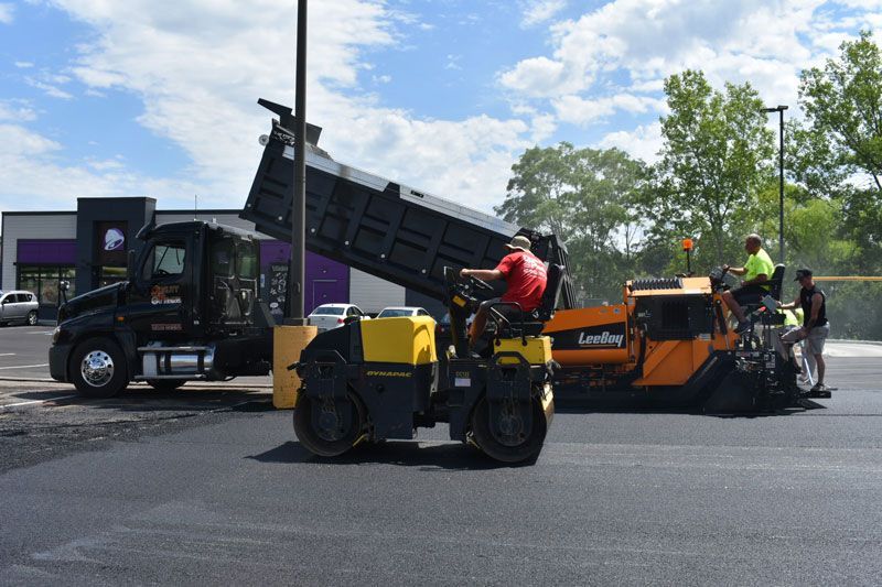 A dump truck is being loaded with asphalt in a parking lot.