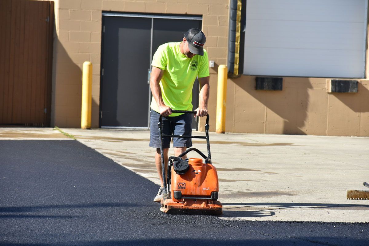 A man is using a machine to compact asphalt in a parking lot.