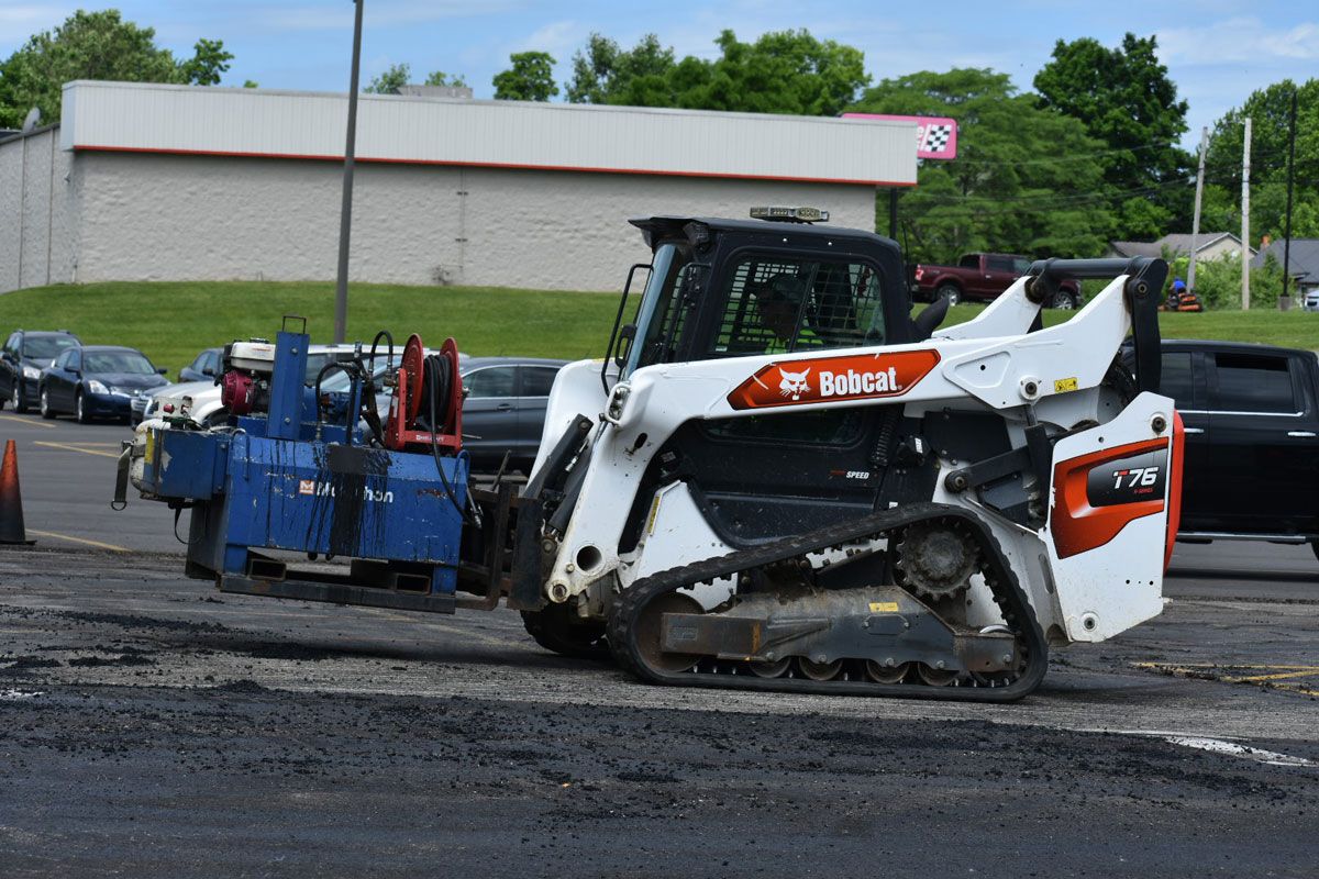 A bobcat is sitting in a parking lot next to a building.