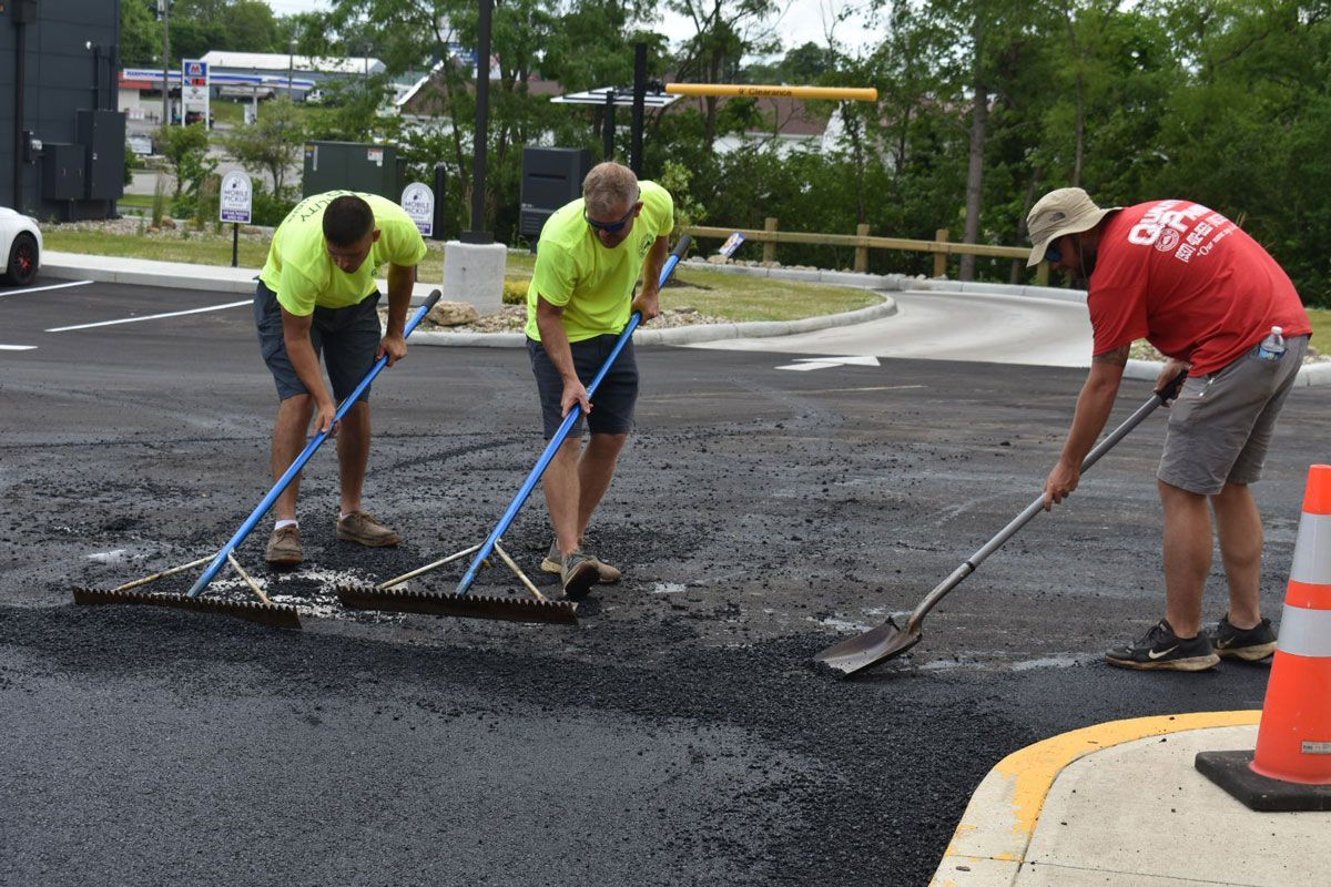 A group of men are working on a road with brooms.