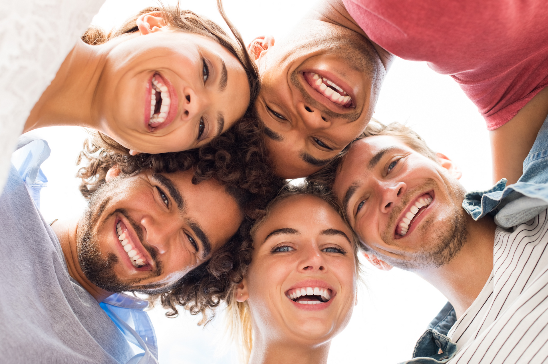 Group of diverse friends, faces close, smiling down at the camera.
