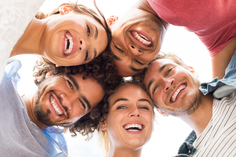 Group of diverse friends, faces close, smiling down at the camera.
