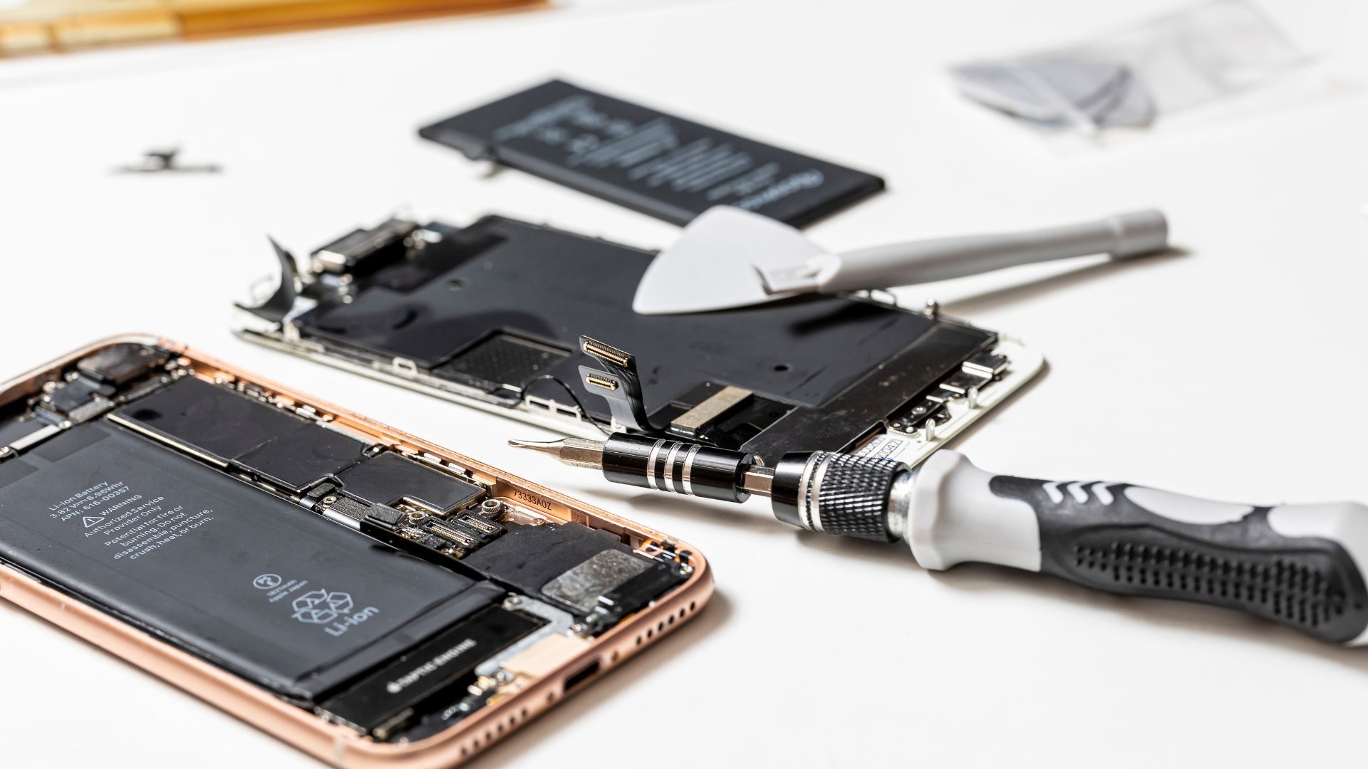 A cell phone is being repaired with tools on a table.