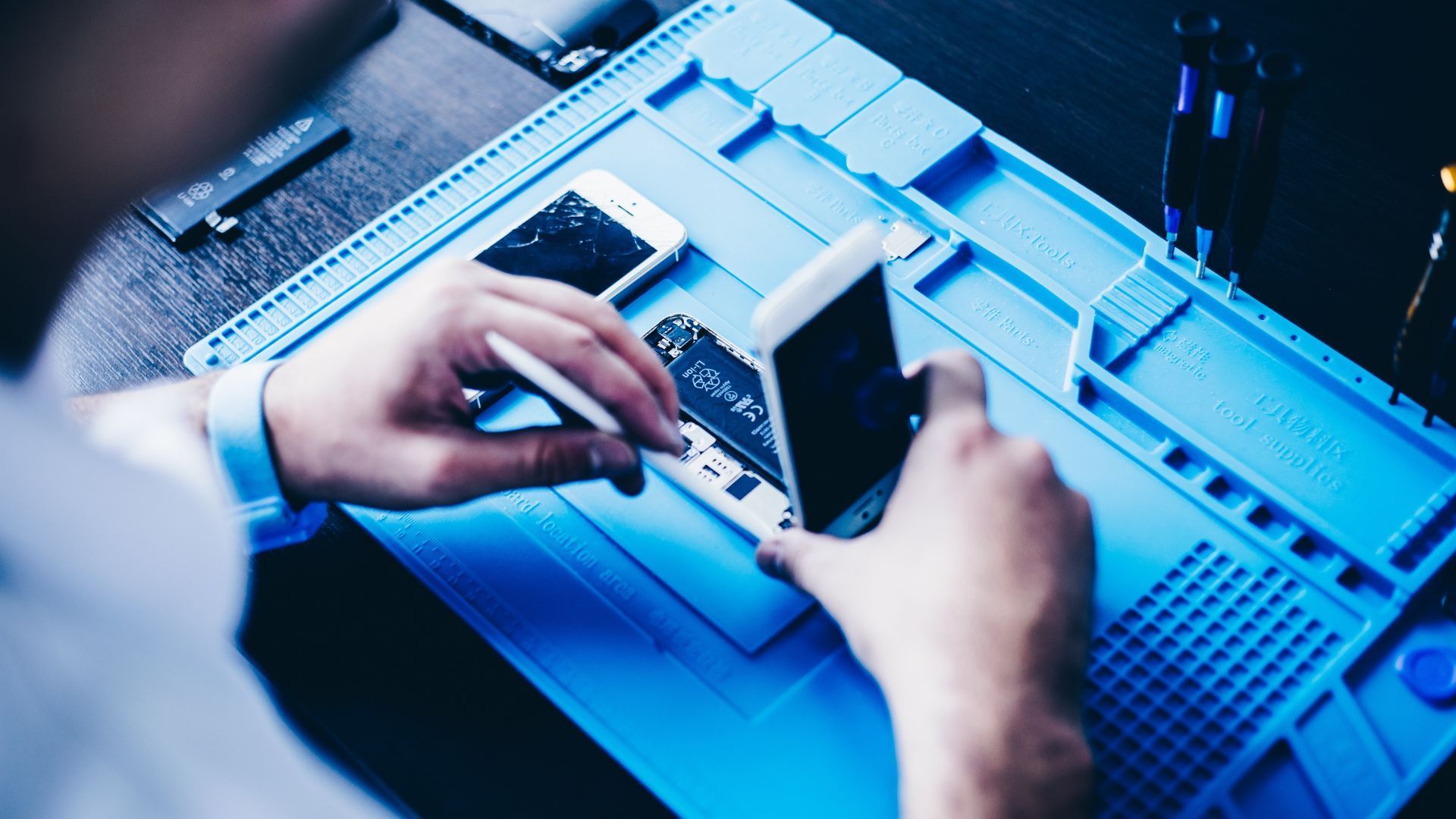 A man is repairing a cell phone on a blue mat.