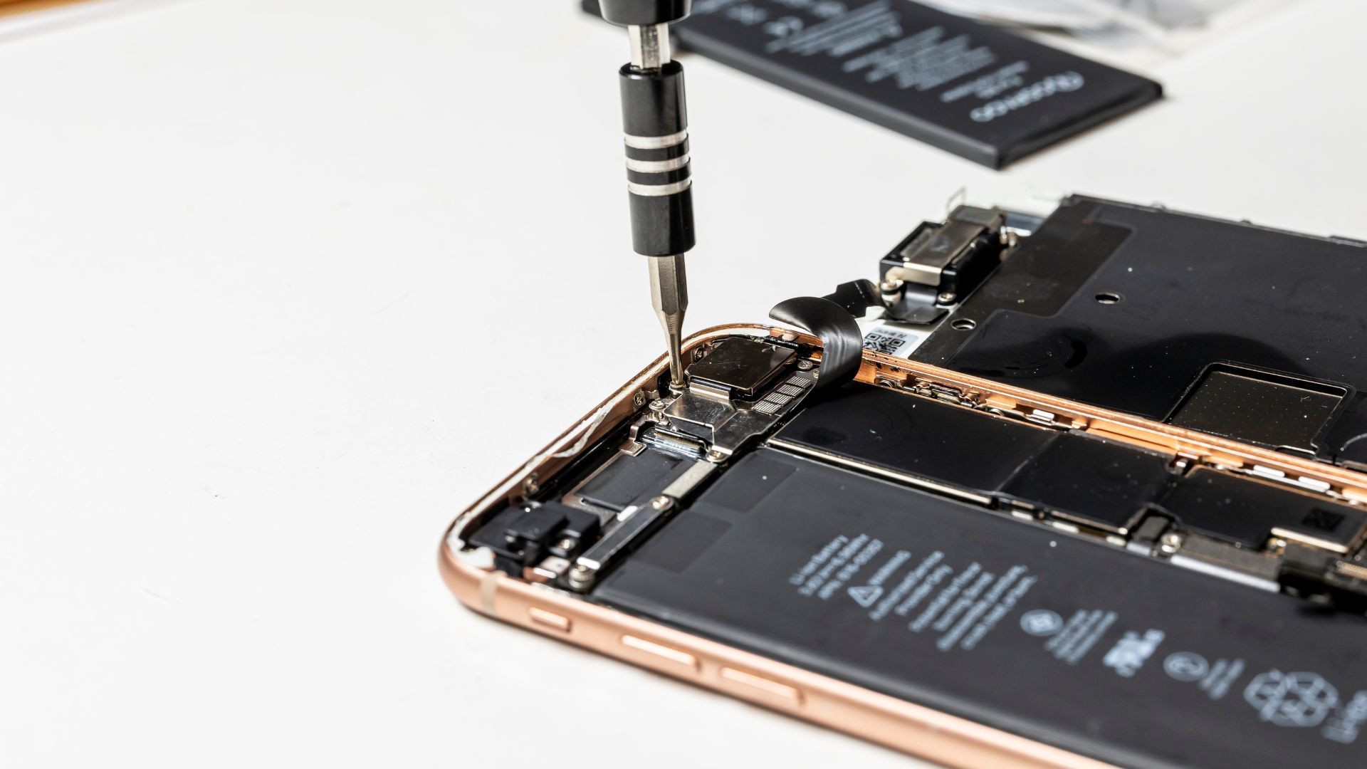 A close up of a cell phone being repaired with a screwdriver.