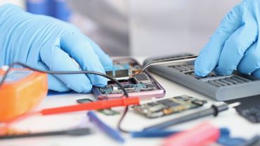 A person wearing blue gloves is working on a cell phone.