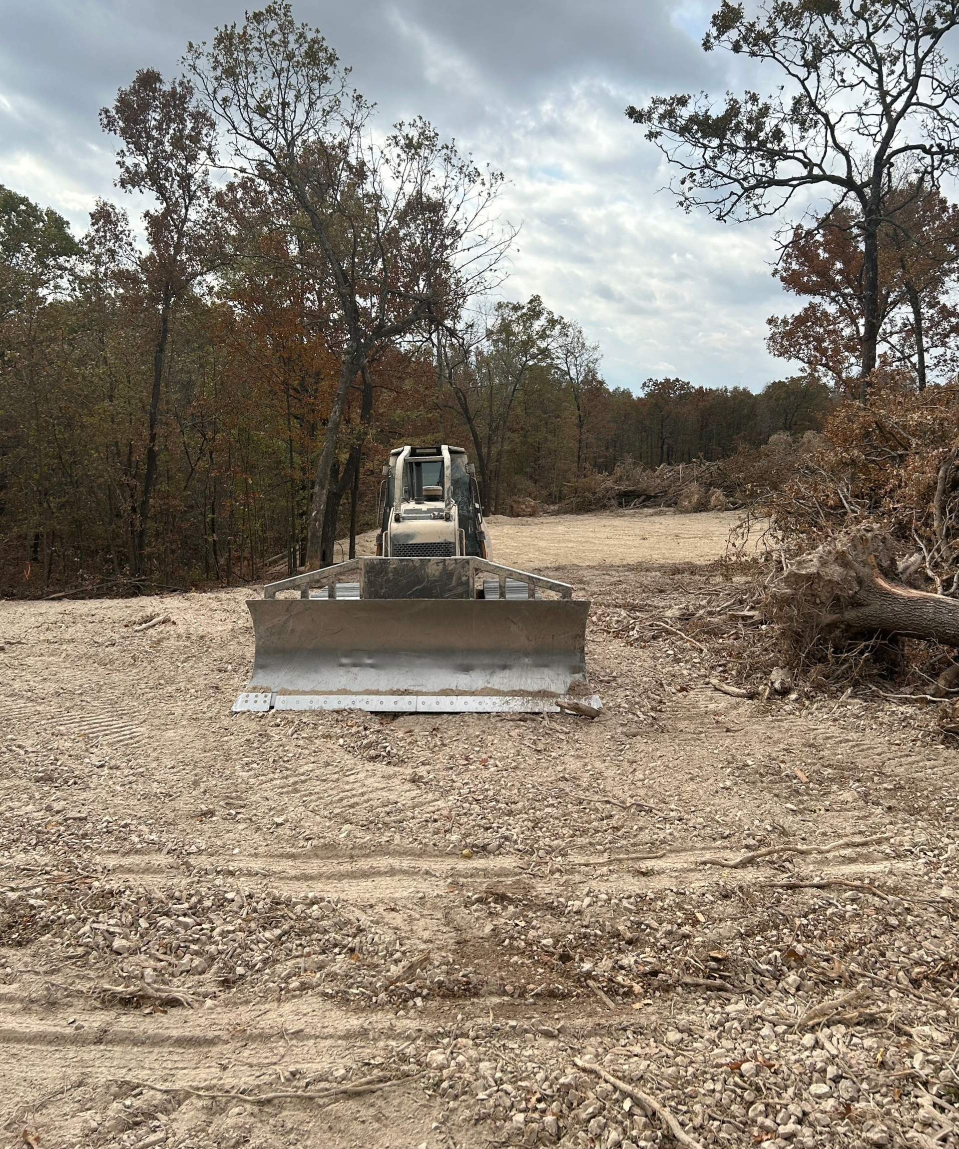 Bulldozer on a cleared construction site, surrounded by trees under a cloudy sky.