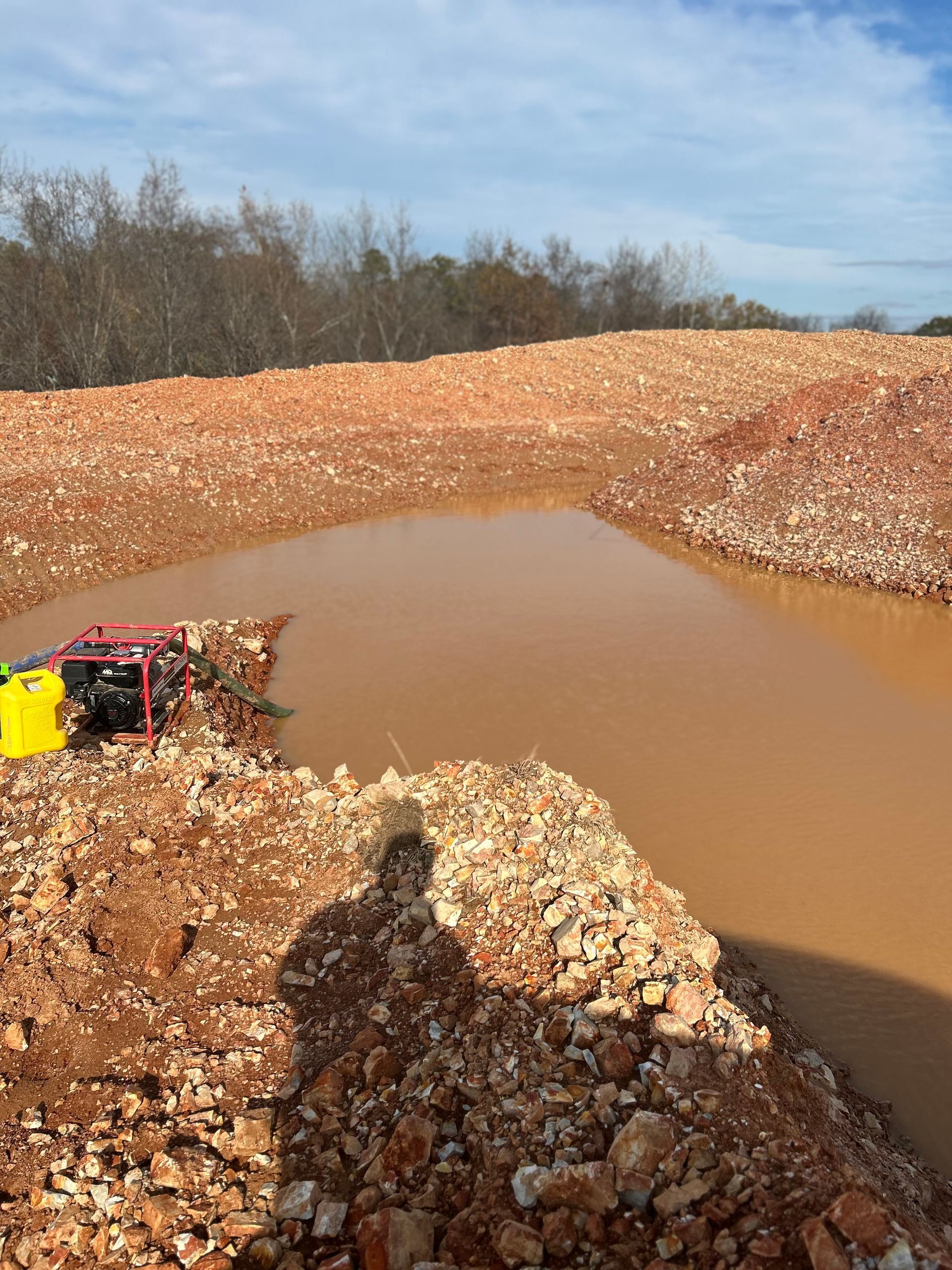 Muddy water pool in a red dirt quarry, with a shadow and equipment visible.