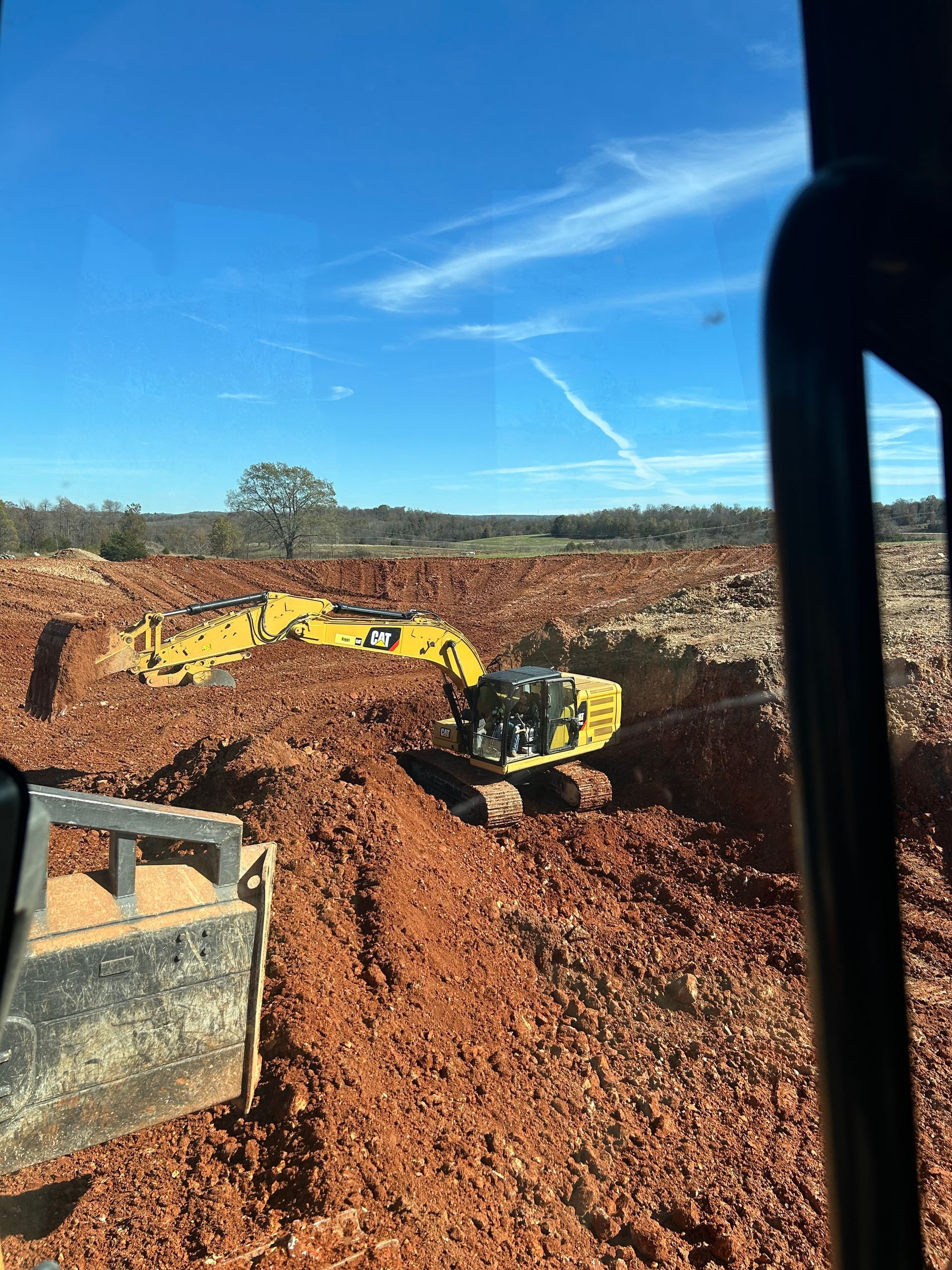 Yellow excavator digging red earth on a construction site under a blue sky.