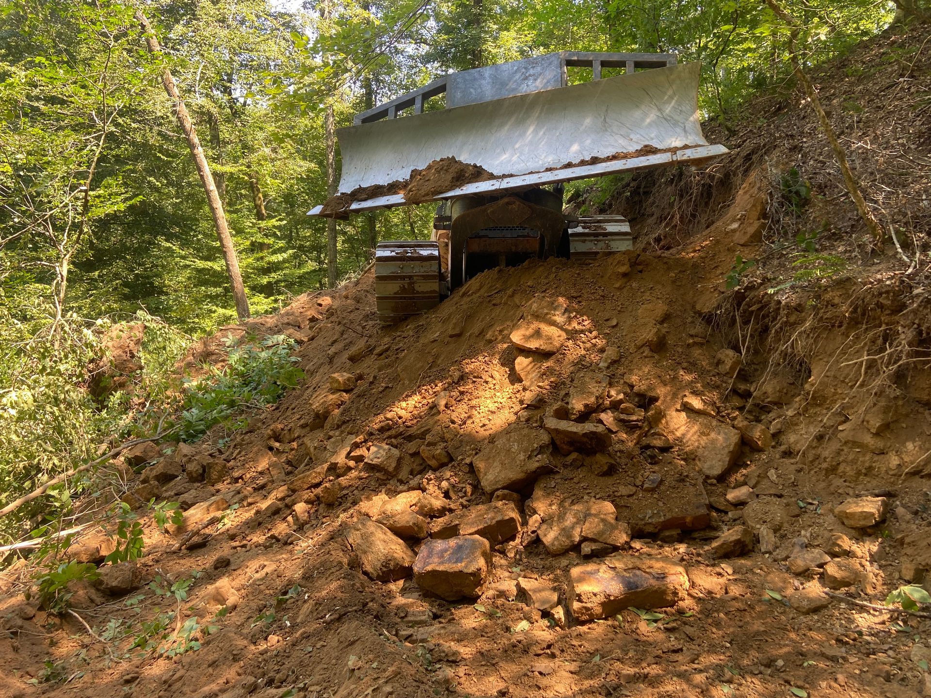 Bulldozer pushing dirt on a hillside in a wooded area.