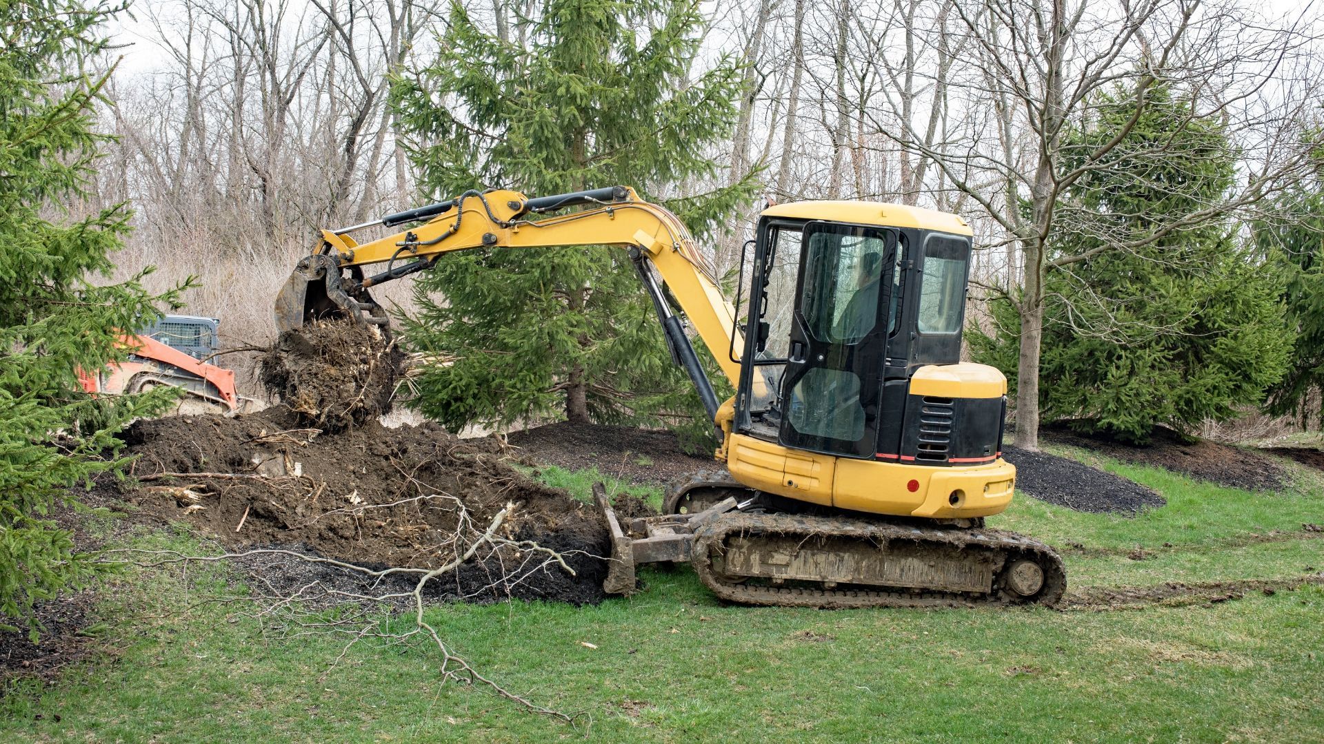 Yellow excavator digging in grassy yard near trees.